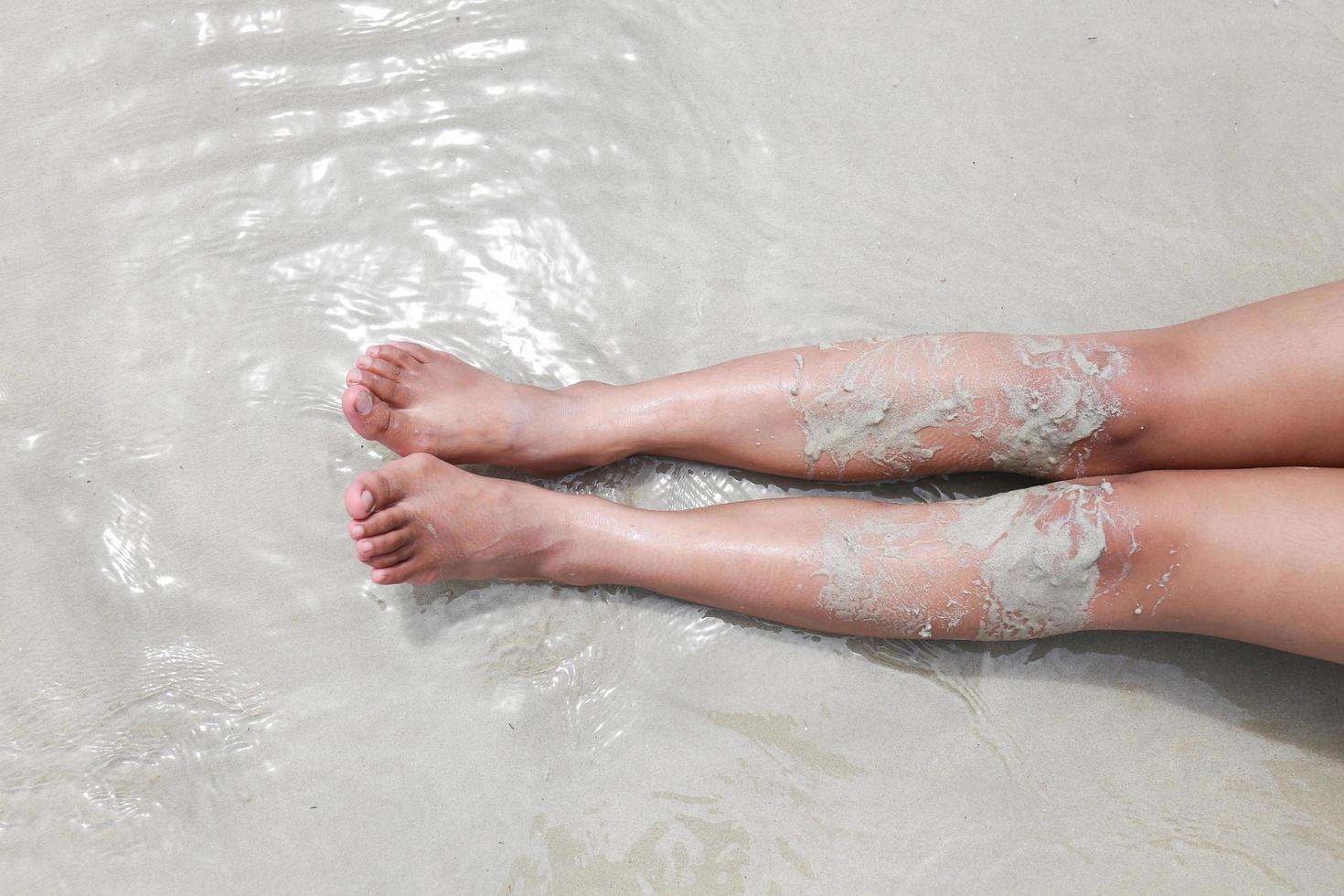 pierna o pies desnudos de mujer en el océano en la playa de arena foto