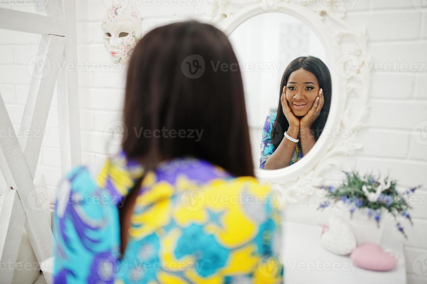 Elegance african american woman model wear in colored clothes. Chic afro women in room looking at mirror. photo