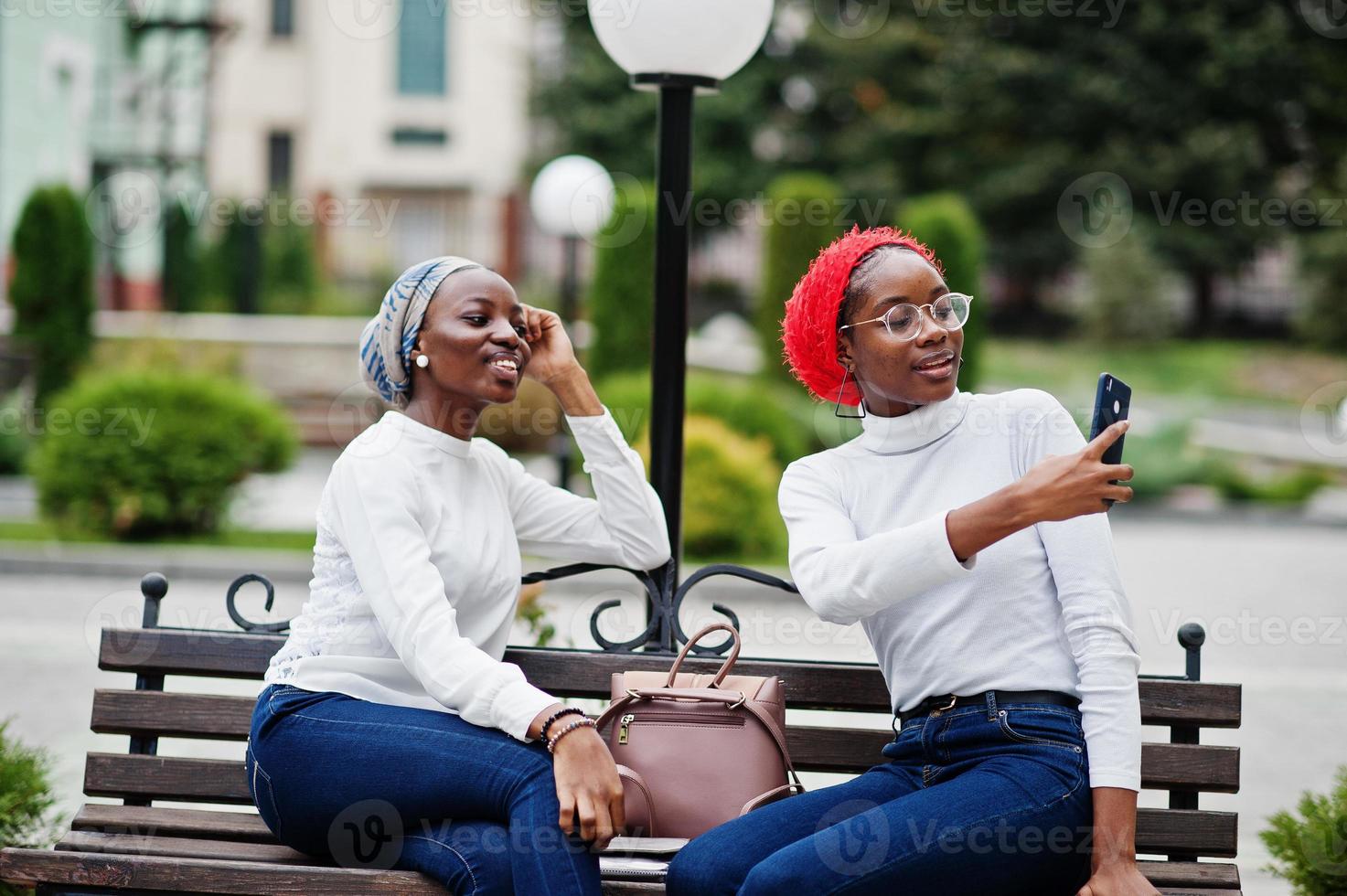 Two young modern fashionable, attractive, tall and slim african muslim womans in hijab or turban head scarf posed together with mobile phones at hands. photo