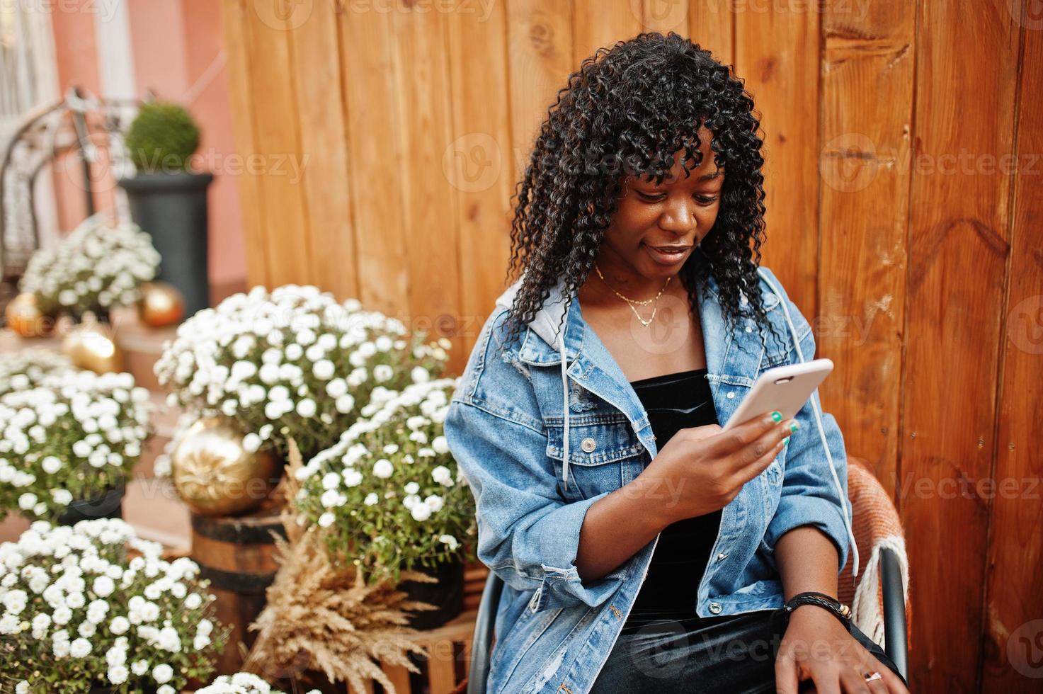 Stylish trendy afro france curly woman posed at autumn day in jeans jacket. Black african female model with mobile phone. photo