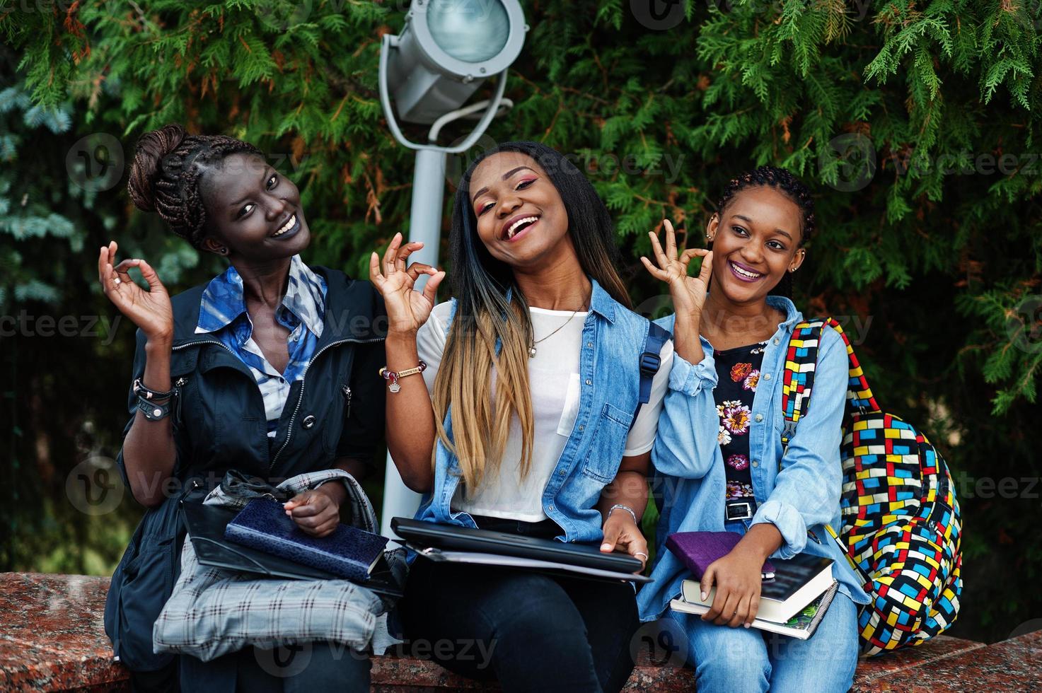 tres estudiantes africanas posaron con mochilas y artículos escolares en el patio de la universidad y muestran el cartel de ok con las manos. foto