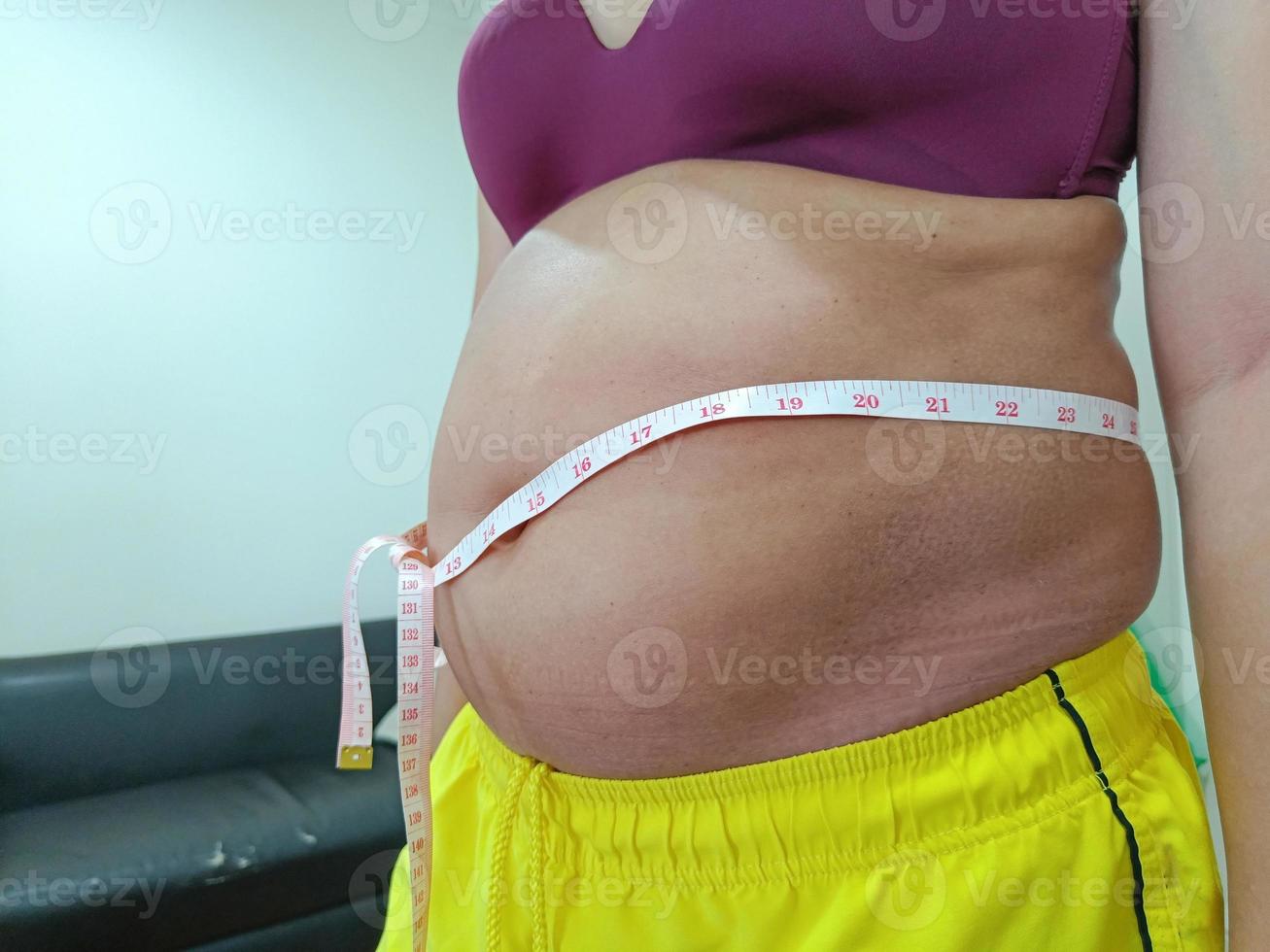vista frontal. mujer asiática gorda en mal estado de pie mostrando su vientre. necesitas cuidar tu salud y hacer ejercicio. foto