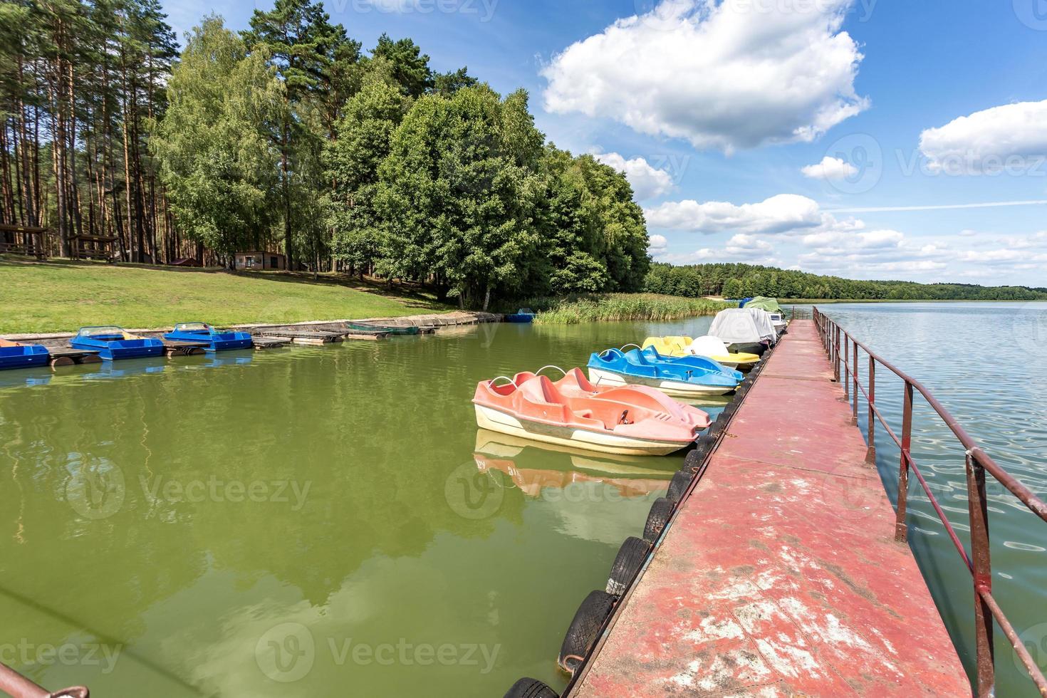 colored old vintage plastic catamarans and boats near a wooden pier on the shore of a large lake photo