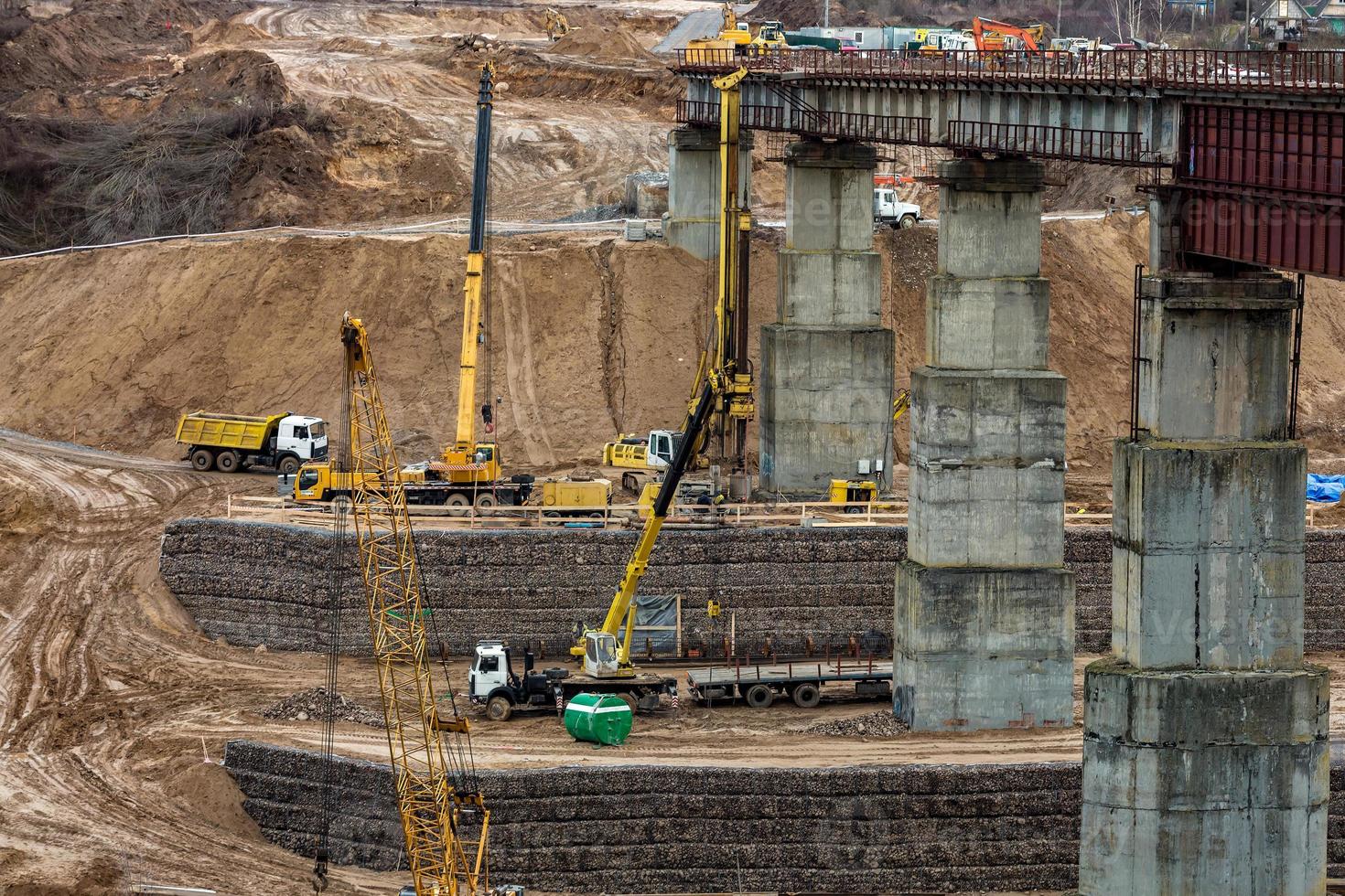 construction or reconstruction of highway concrete bridge over a wide river. construction machinery, trucks and cranes work photo