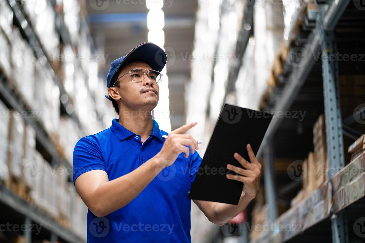 trabajador asiático feliz en uniforme azul con portapapeles en almacén. trabajadores felices en el centro de distribución. cadena de suministro y concepto de tecnología de red logística. foto