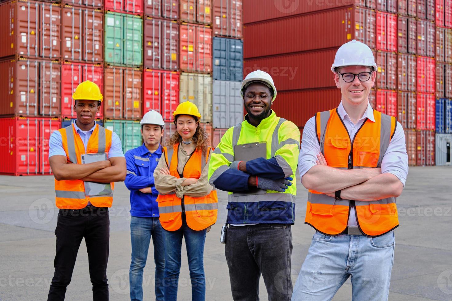 Portrait of a group of multiracial workers team in safety uniforms, arms crossed and looking at camera at logistics dock with many stacks of containers, shipping goods, cargo transportation industry. photo
