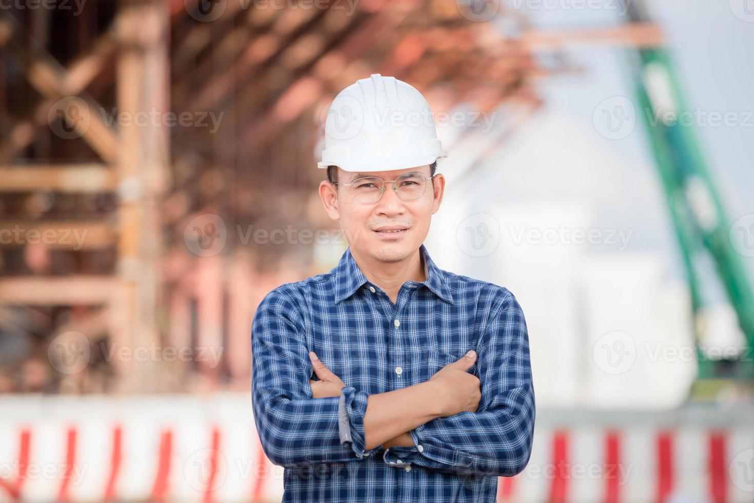 hombre trabajador con el brazo cruzado mirando la cámara, ingeniero revisando el proyecto en el sitio de construcción, hombre con casco en el sitio de construcción de infraestructura foto