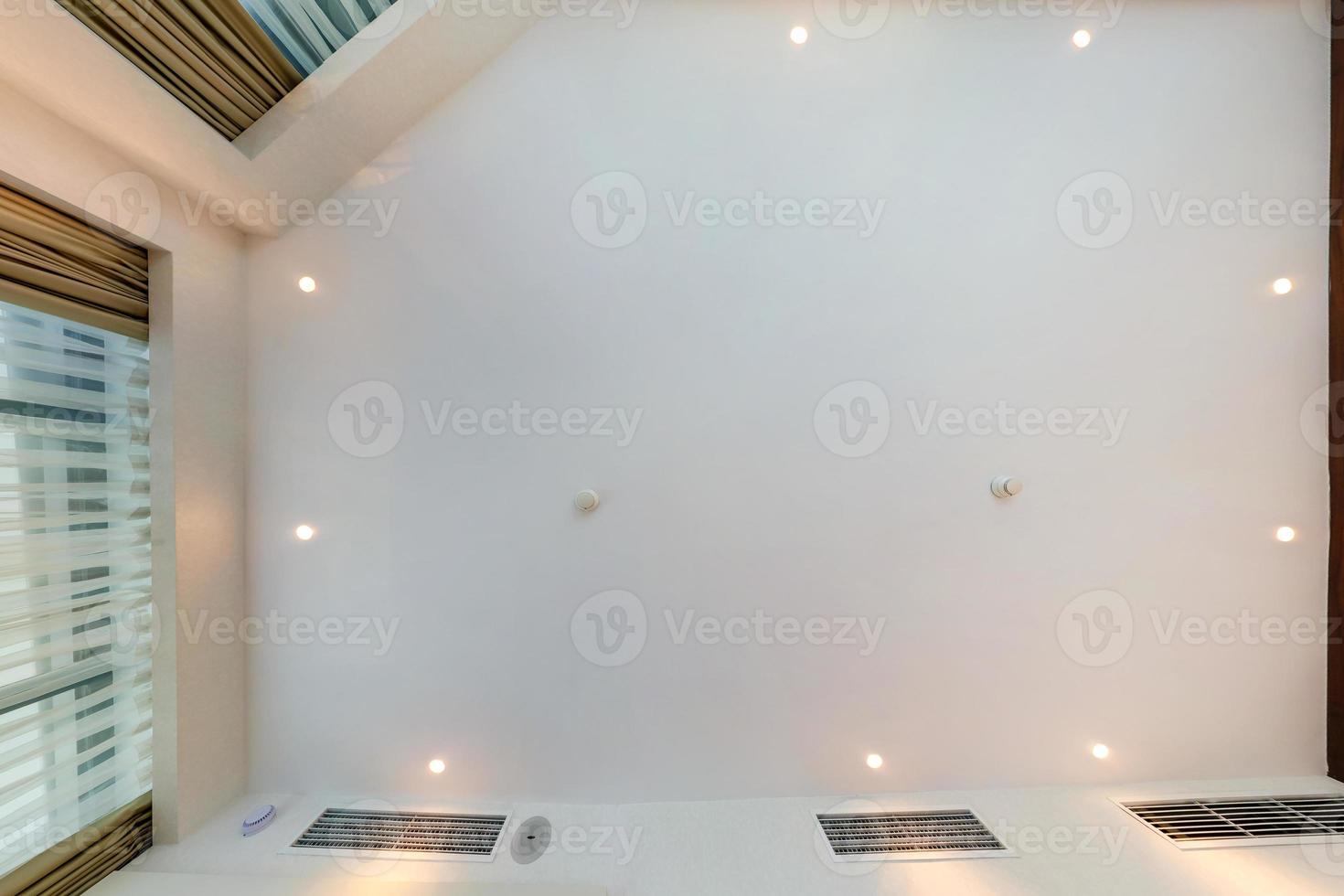 look up on suspended ceiling with halogen spots lamps and drywall construction with fire alarm sensor in empty room in apartment or house. Stretch ceiling photo