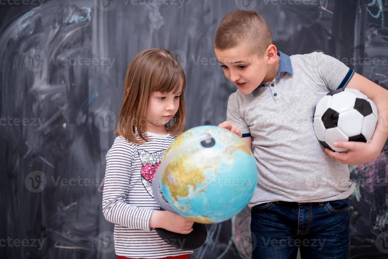 niño y niña usando el globo terráqueo frente a la pizarra foto