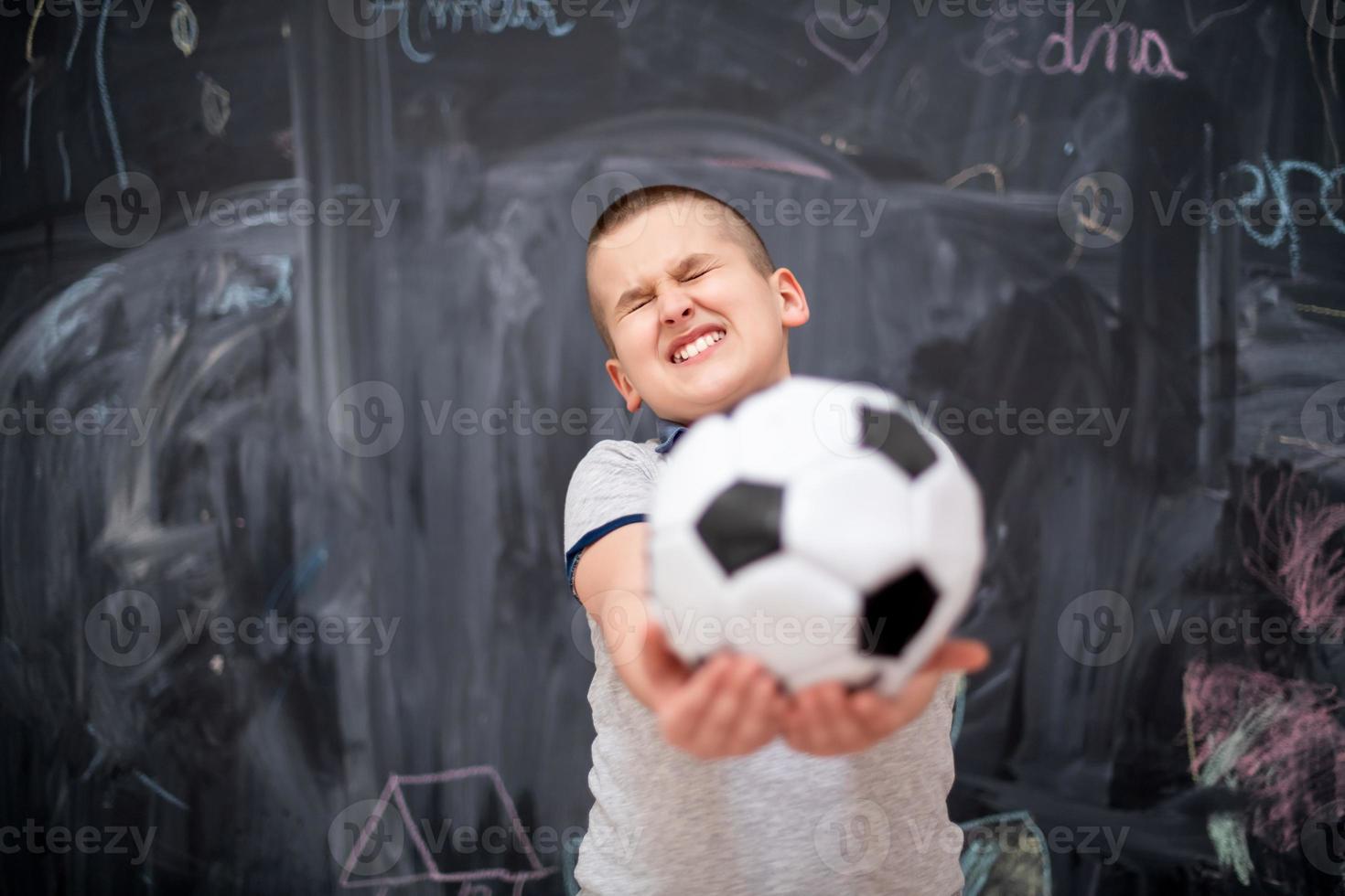 niño feliz sosteniendo una pelota de fútbol frente a la pizarra foto