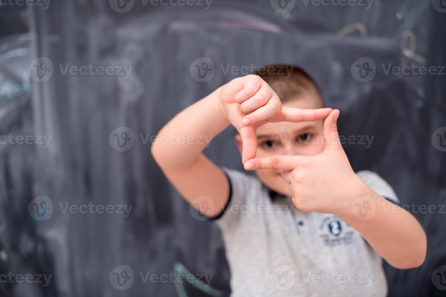 happy boy making hand frame gesture in front of chalkboard photo