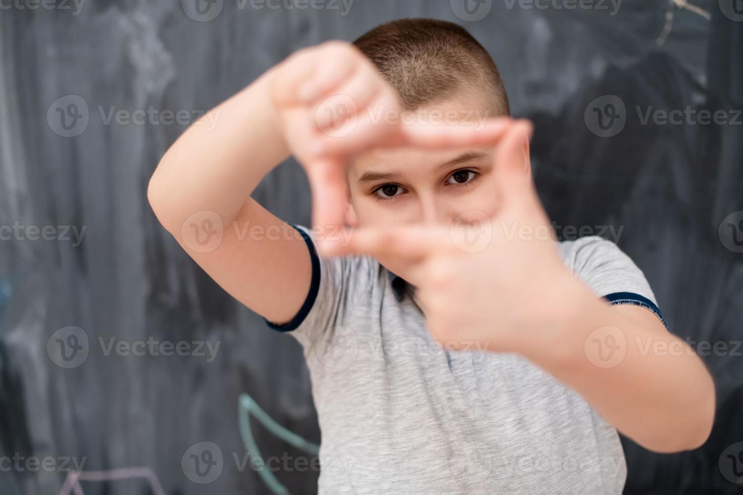 happy boy making hand frame gesture in front of chalkboard photo