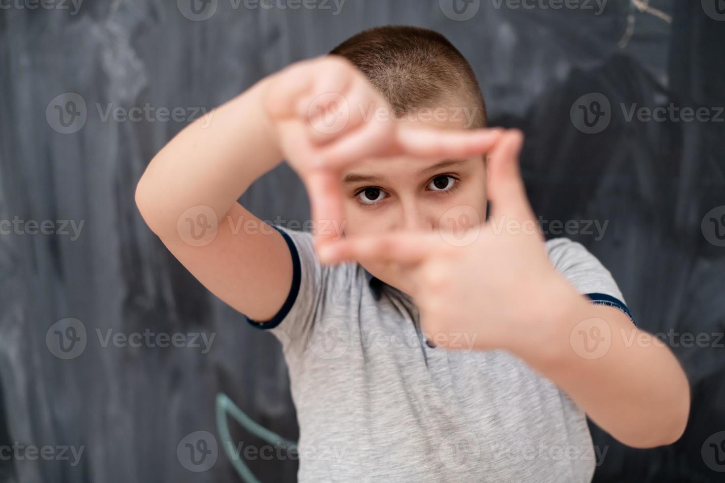 niño feliz haciendo gesto de marco de mano frente a la pizarra foto