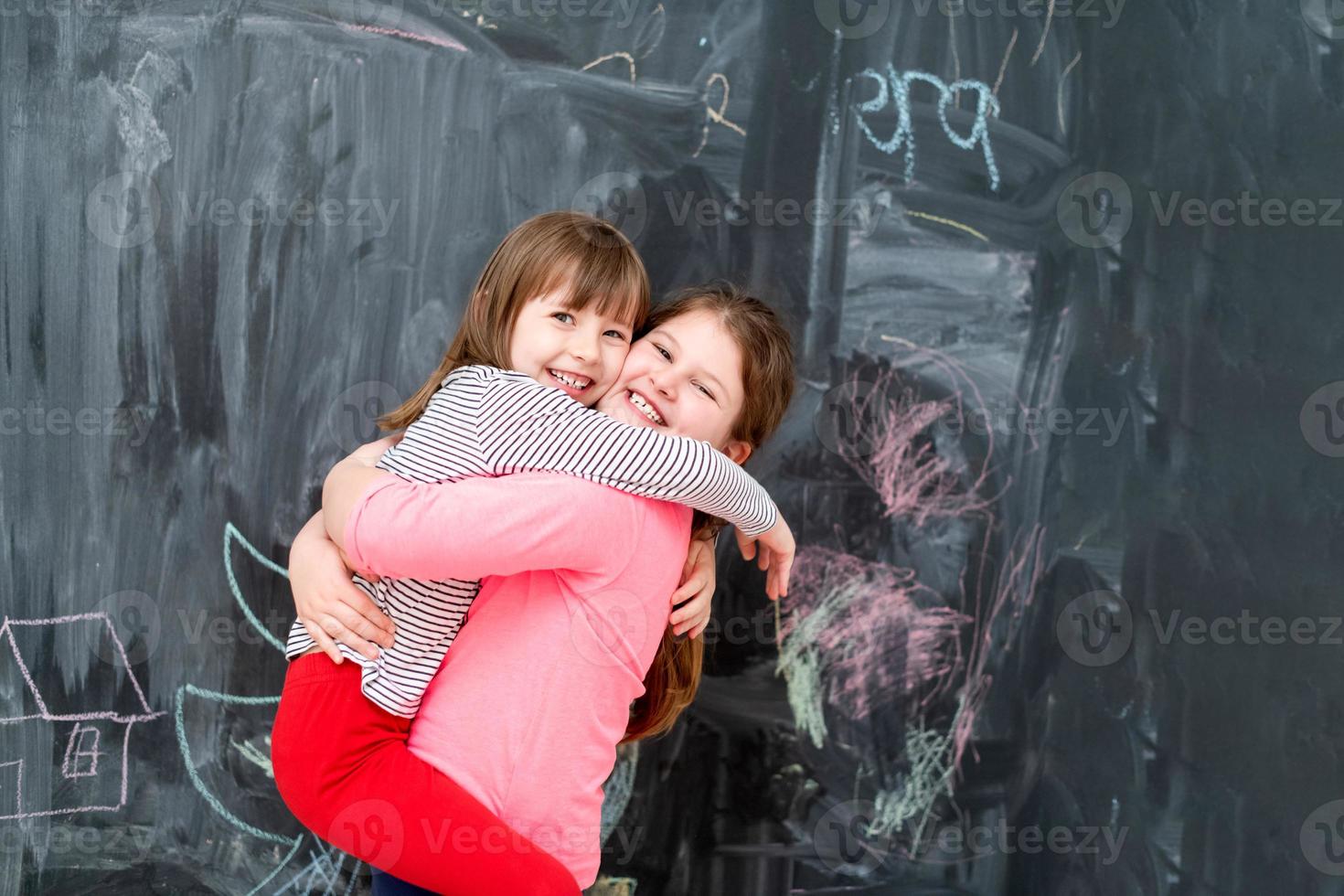 little girls hugging in front of chalkboard photo