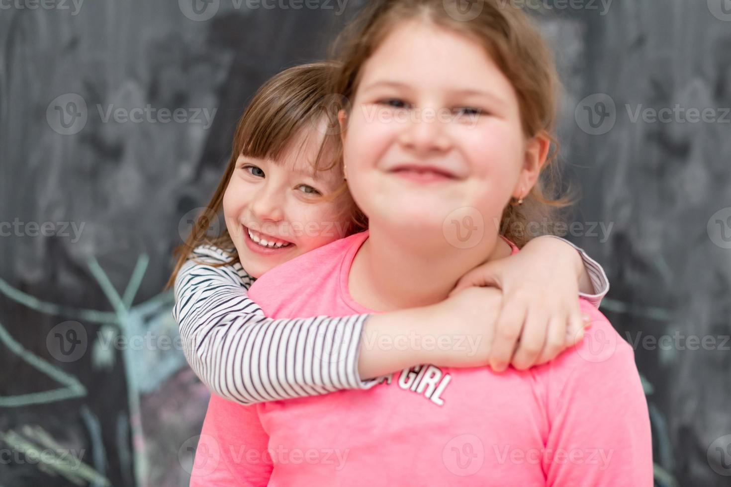 little girls hugging in front of chalkboard photo