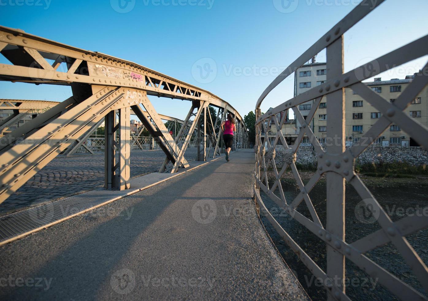 woman jogging across the bridge at sunny morning photo
