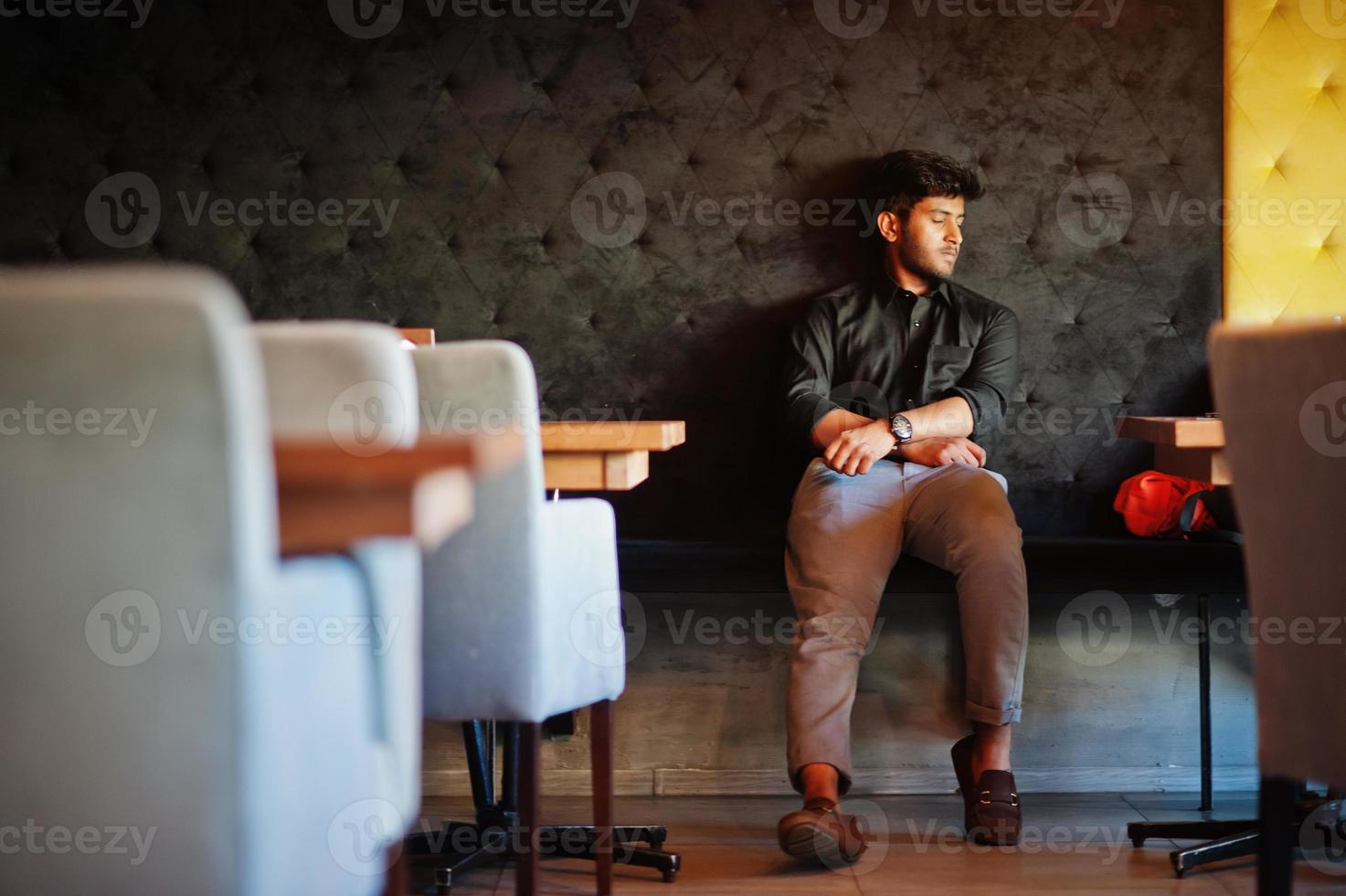 cansado después del trabajo. un joven indio confiado con camisa negra sentado en un café y durmiendo. foto