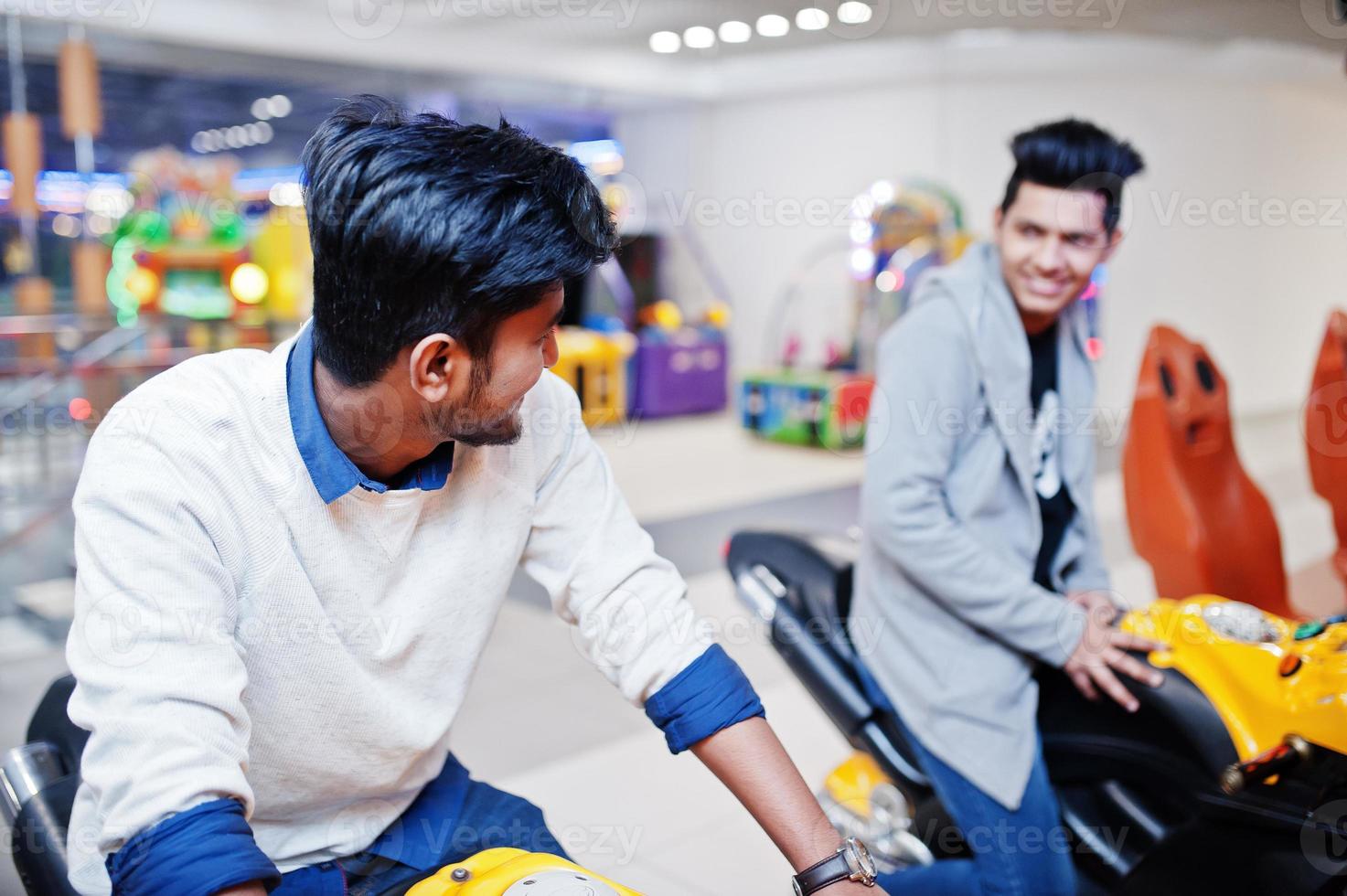 dos chicos asiáticos compiten en la máquina simuladora de carreras de motos del juego arcade de speed rider. foto