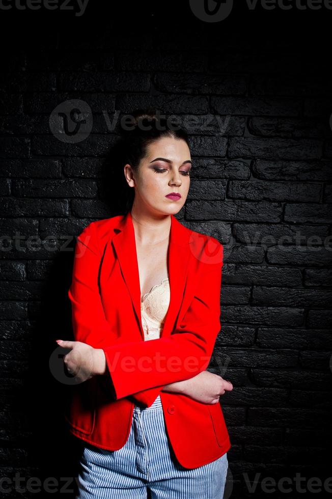 chica morena con estilo en chaqueta roja contra la pared de ladrillo negro de estudio. foto