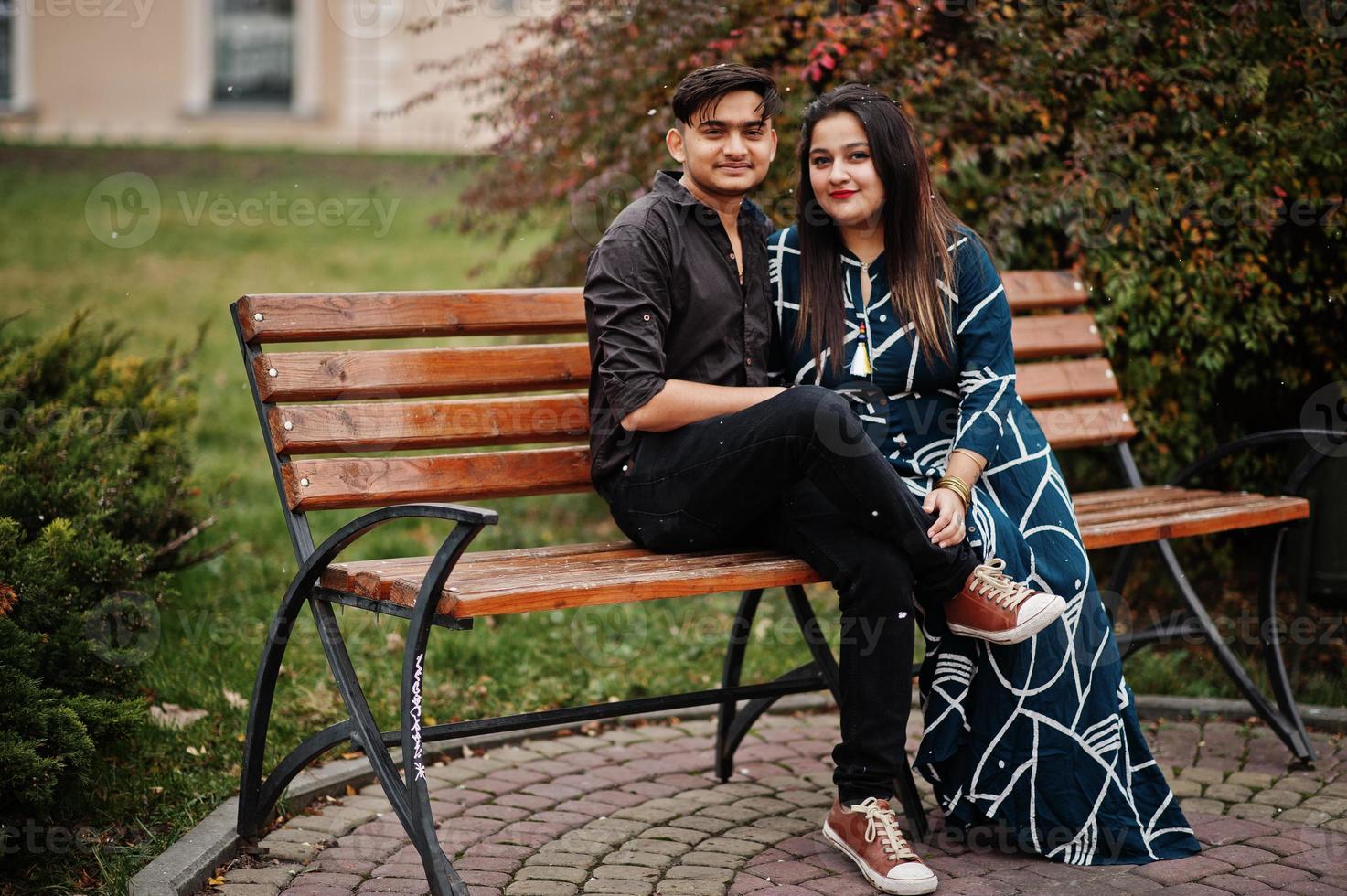 Love story of indian couple posed outdoor, sitting on bench together. photo