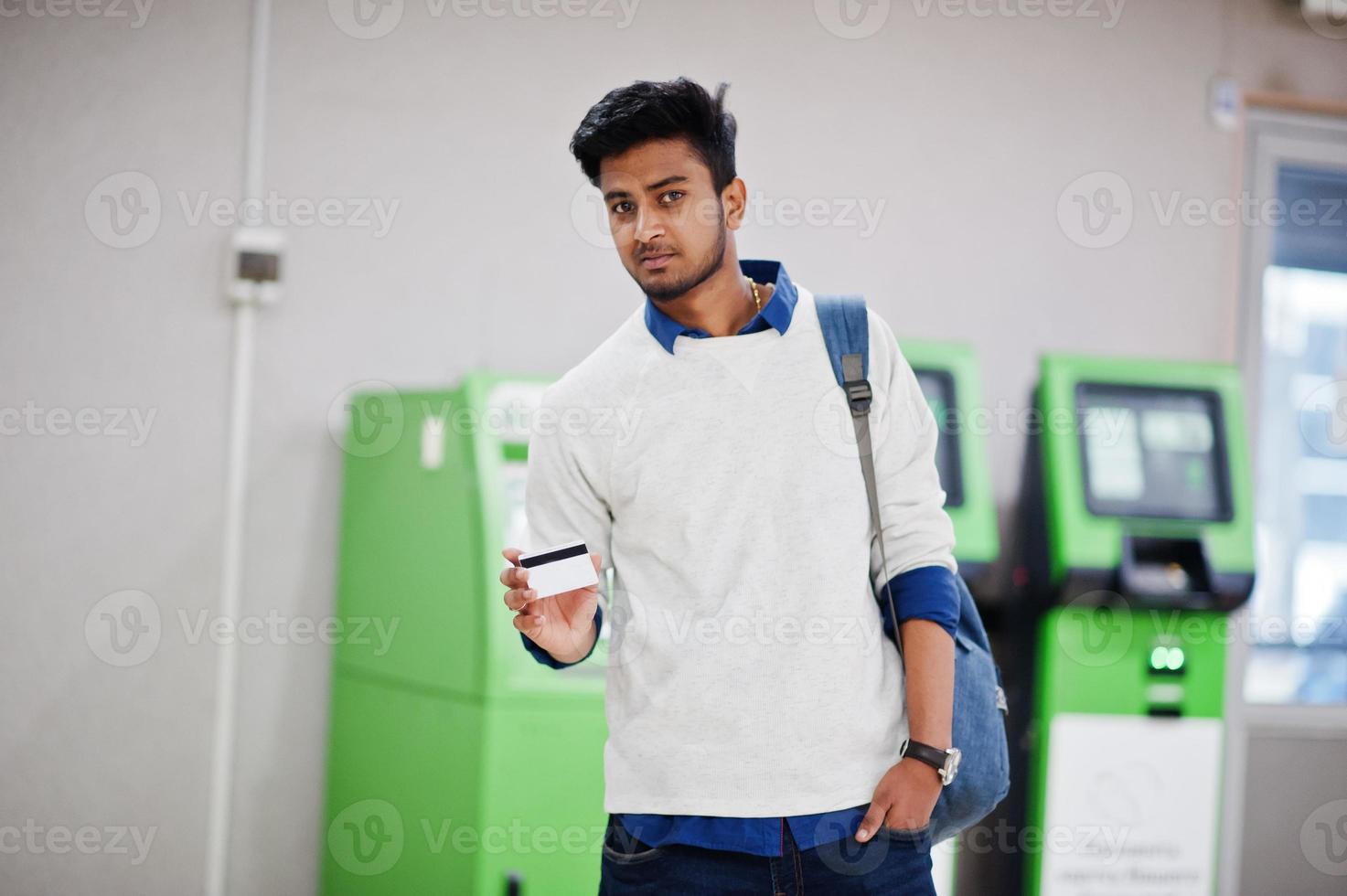 Young stylish asian man with credit card and backpack against row of green ATM. photo
