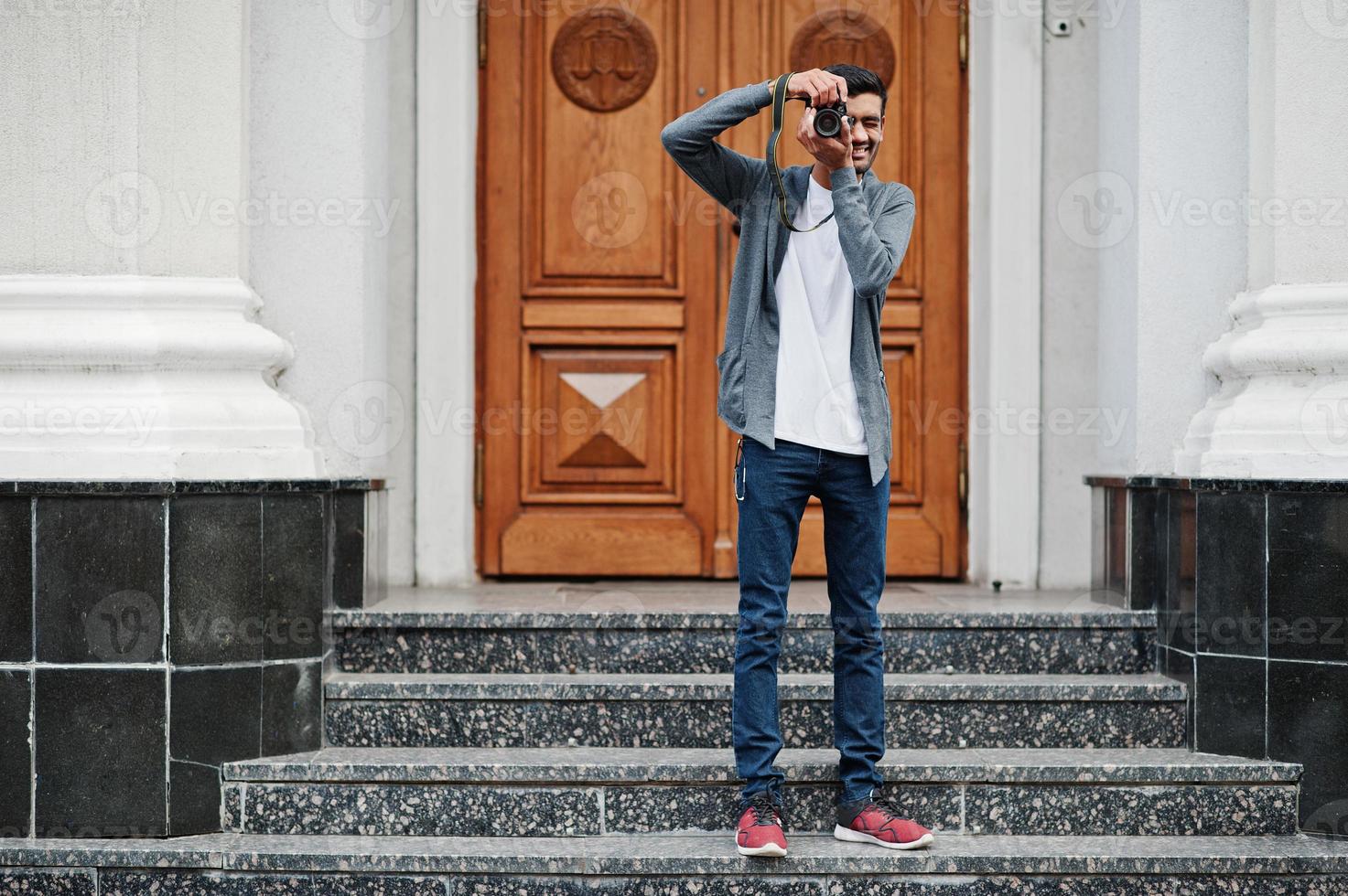 Stylish indian young man photographer wear casual posed outdoor with dslr photo camera at hands.