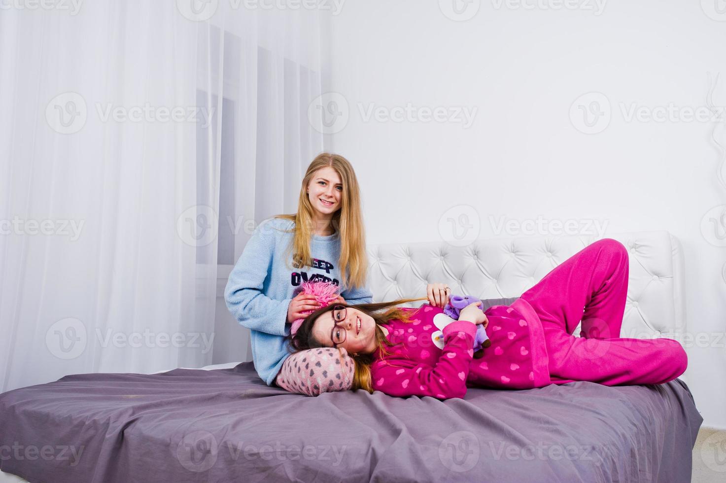Two friends girls in pajamas having fun on bed at room. photo