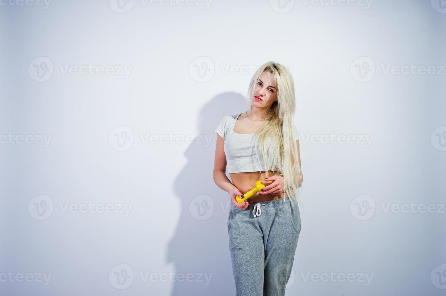 chica rubia deportiva con mancuerna amarilla posada en el estudio sobre fondo blanco. foto