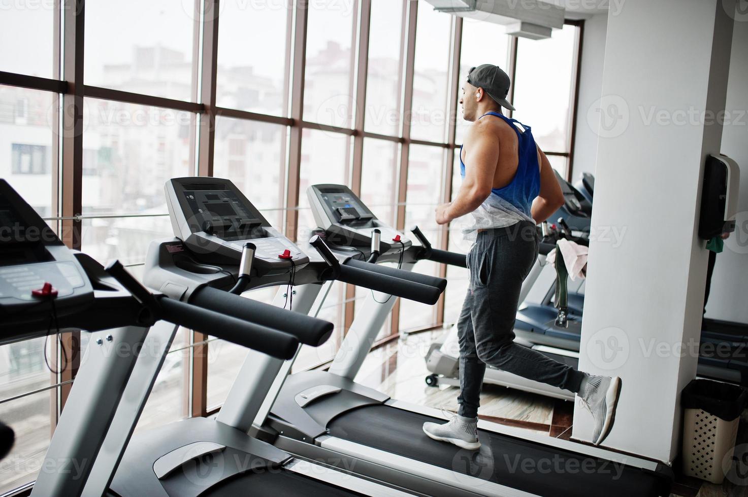Fit and muscular arabian man running on treadmill in gym. photo