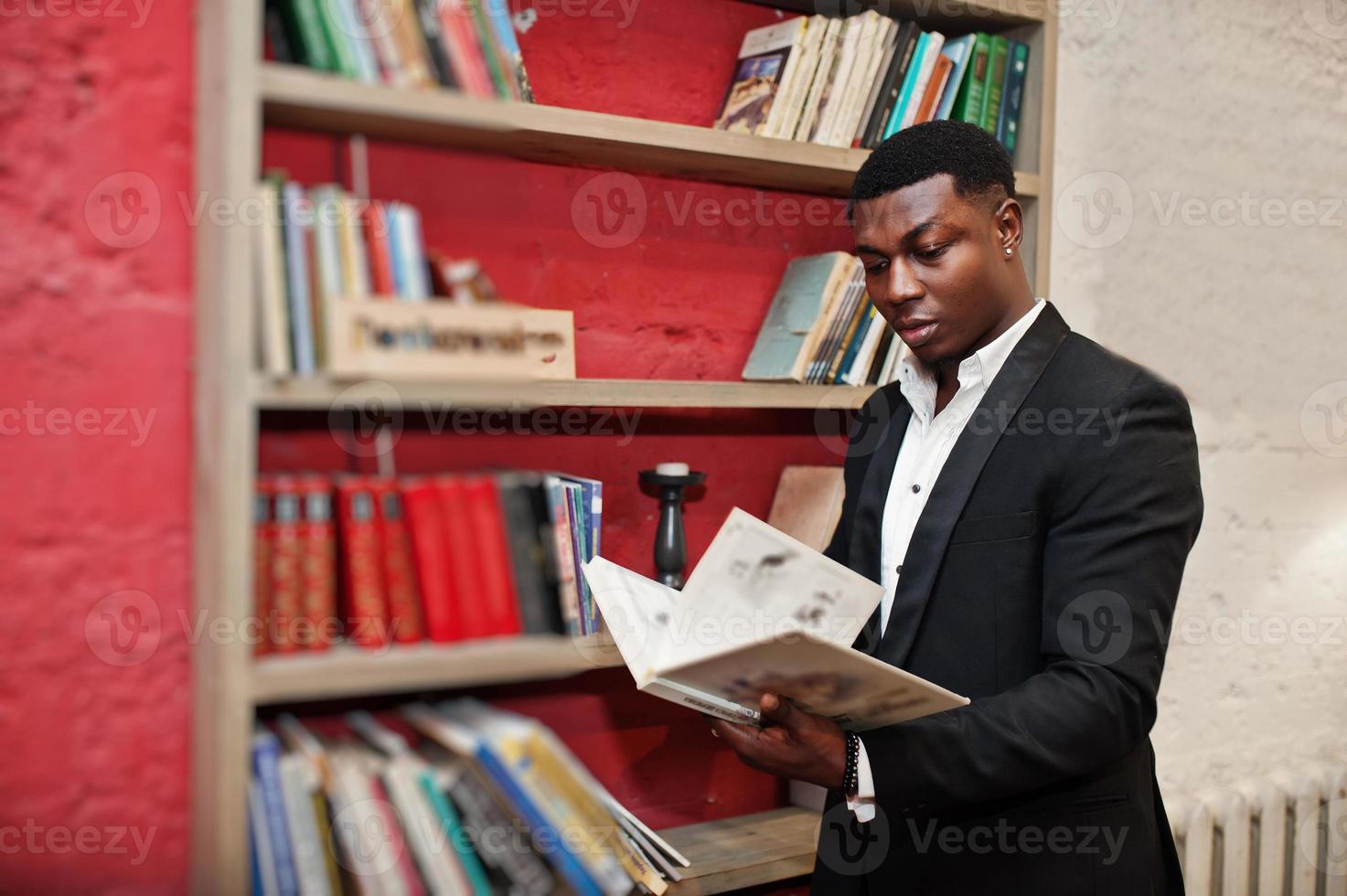 Strong powerful african american man in black suit read book against shelves in free books anti cafe. photo