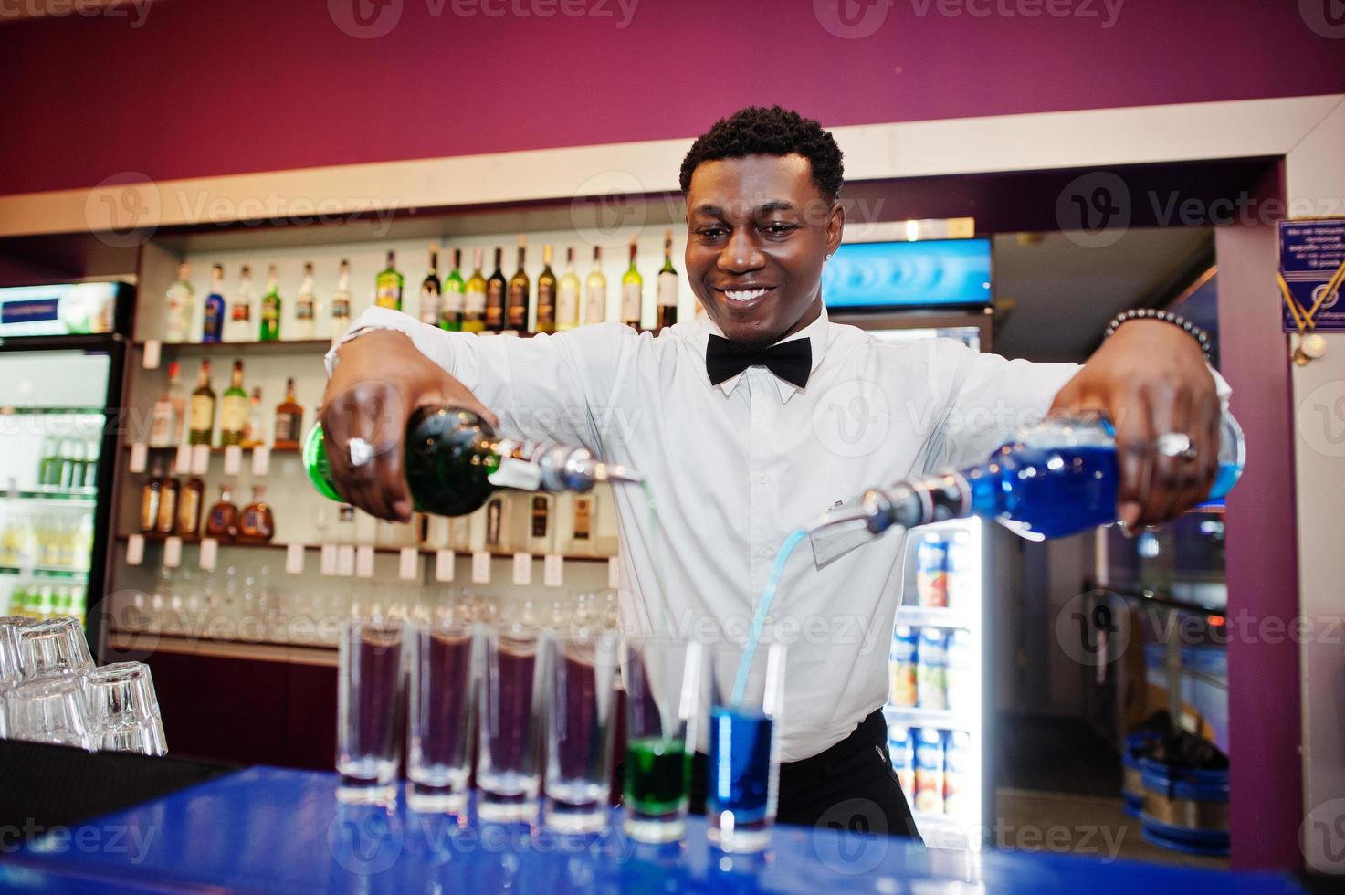 African american bartender at bar making coctails on shots. Alcoholic beverage preparation. photo