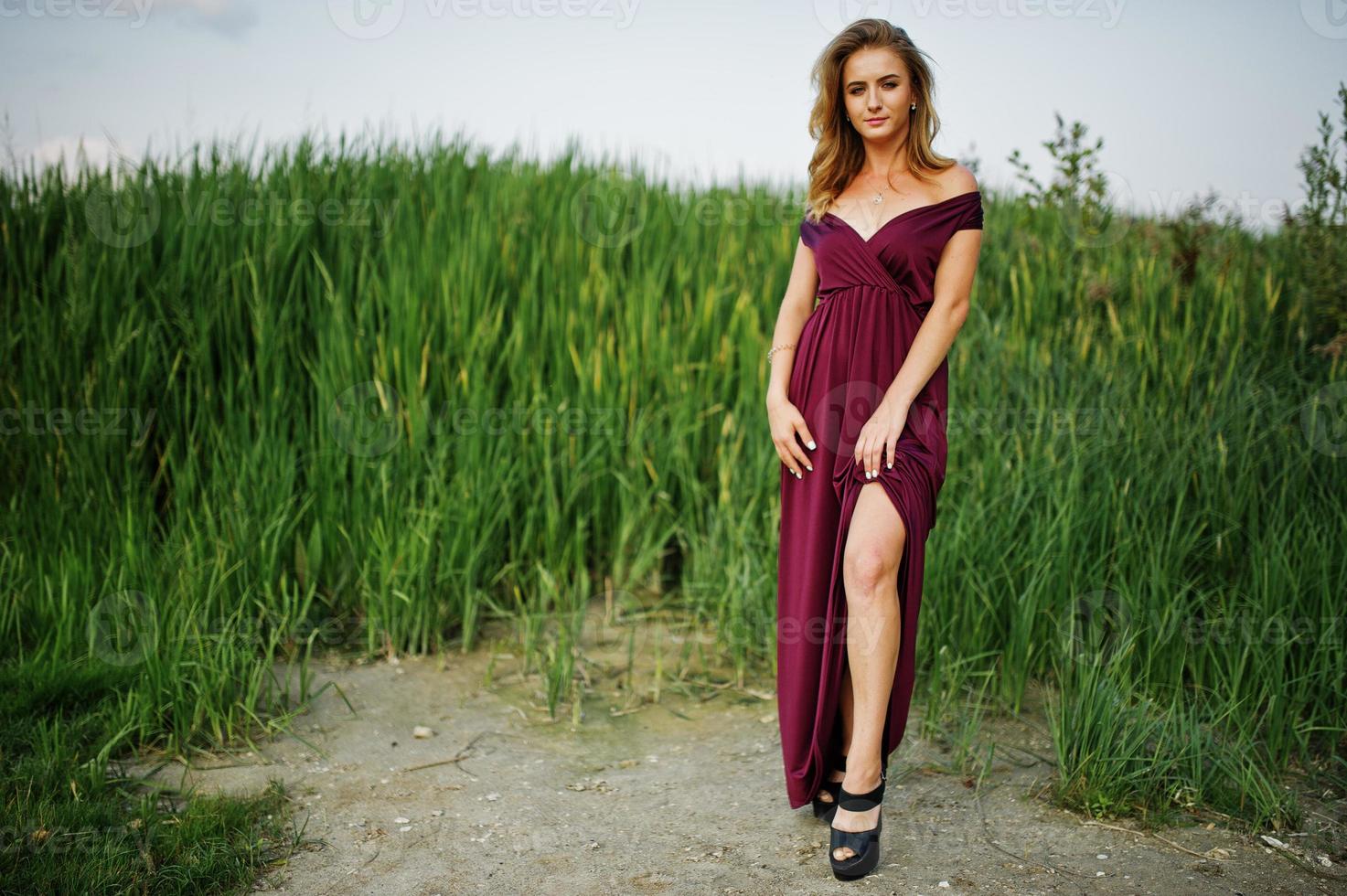 Blonde sensual woman in red marsala dress posing in the reeds. photo