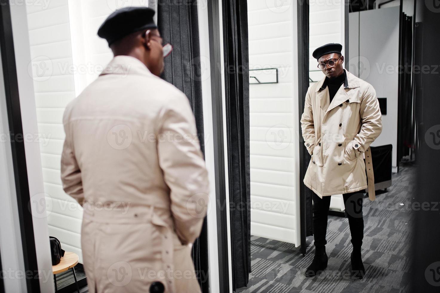 Elegante hombre afroamericano casual con boina negra y impermeable de  trinchera blanca en la tienda de ropa de la sala de montaje, mirando al  espejo. 10414123 Foto de stock en Vecteezy