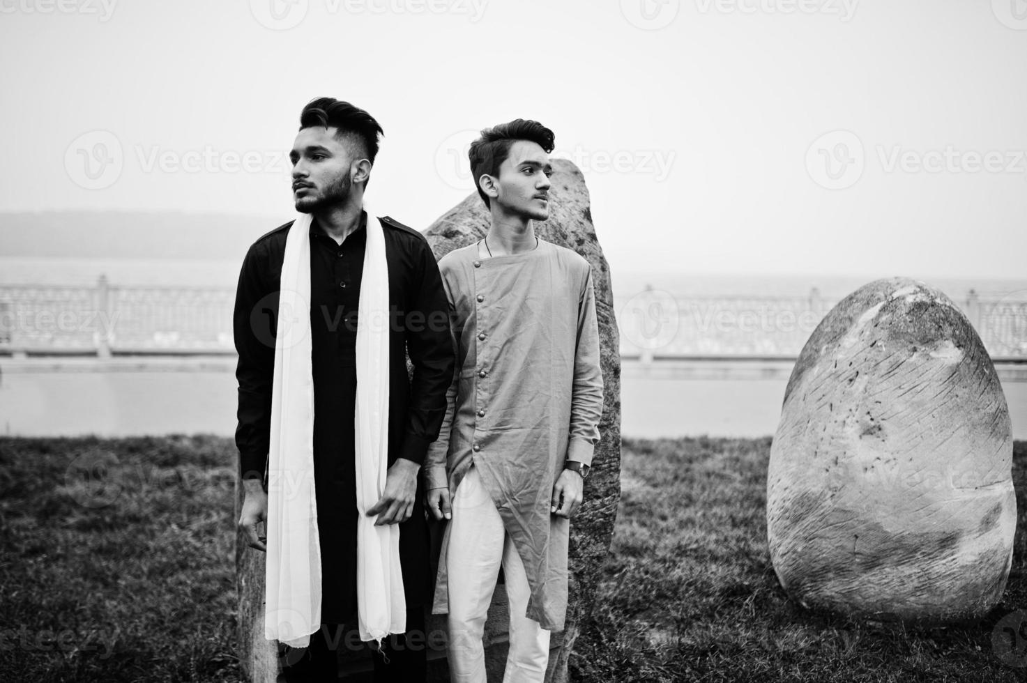 Two indian stylish mans friends in traditional clothes posed outdoor against big stones. photo