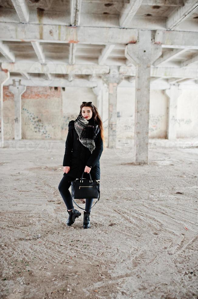 Brunette stylish casual girl in scarf and handbag against abandoned factory place. photo