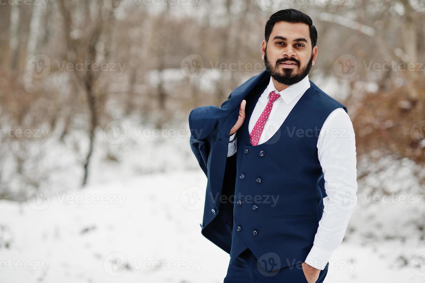 elegante hombre de negocios de barba india con chaleco y traje posado en el día de invierno al aire libre. foto