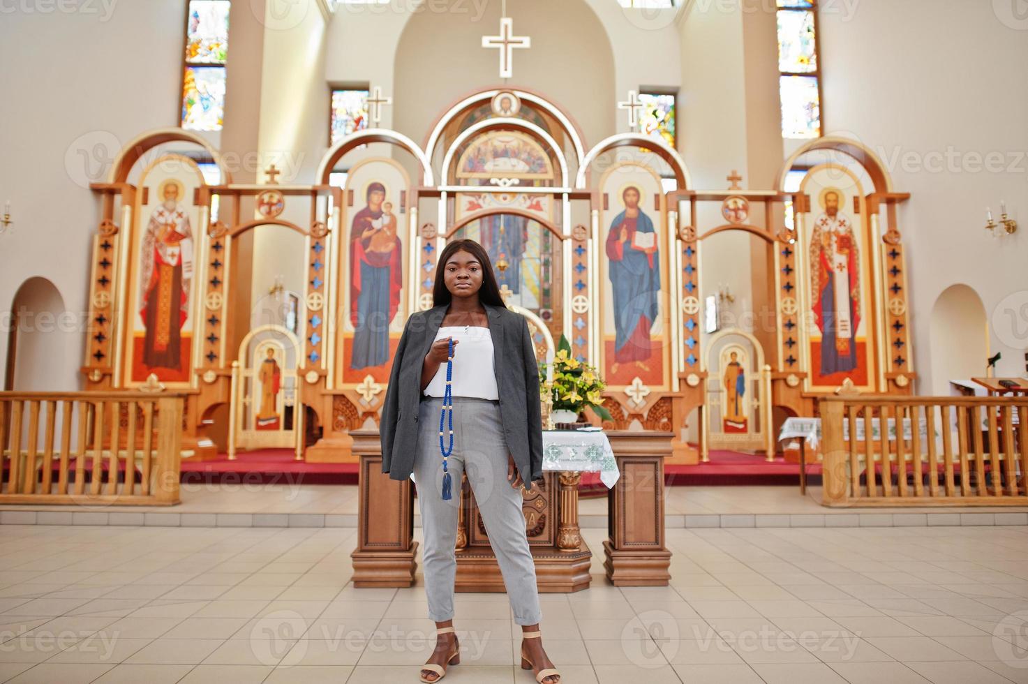 mujer afroamericana rezando en la iglesia. los creyentes meditan en la catedral y tiempo espiritual de oración. chica afro con rosario en las manos. foto