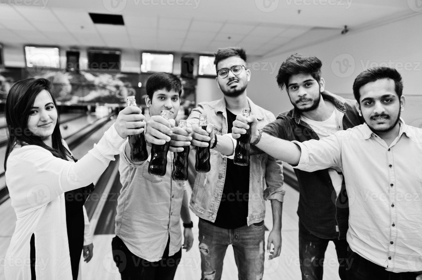 Group of five south asian peoples having rest and fun at bowling club. Clinking cold soda drinks from glass bottles. photo