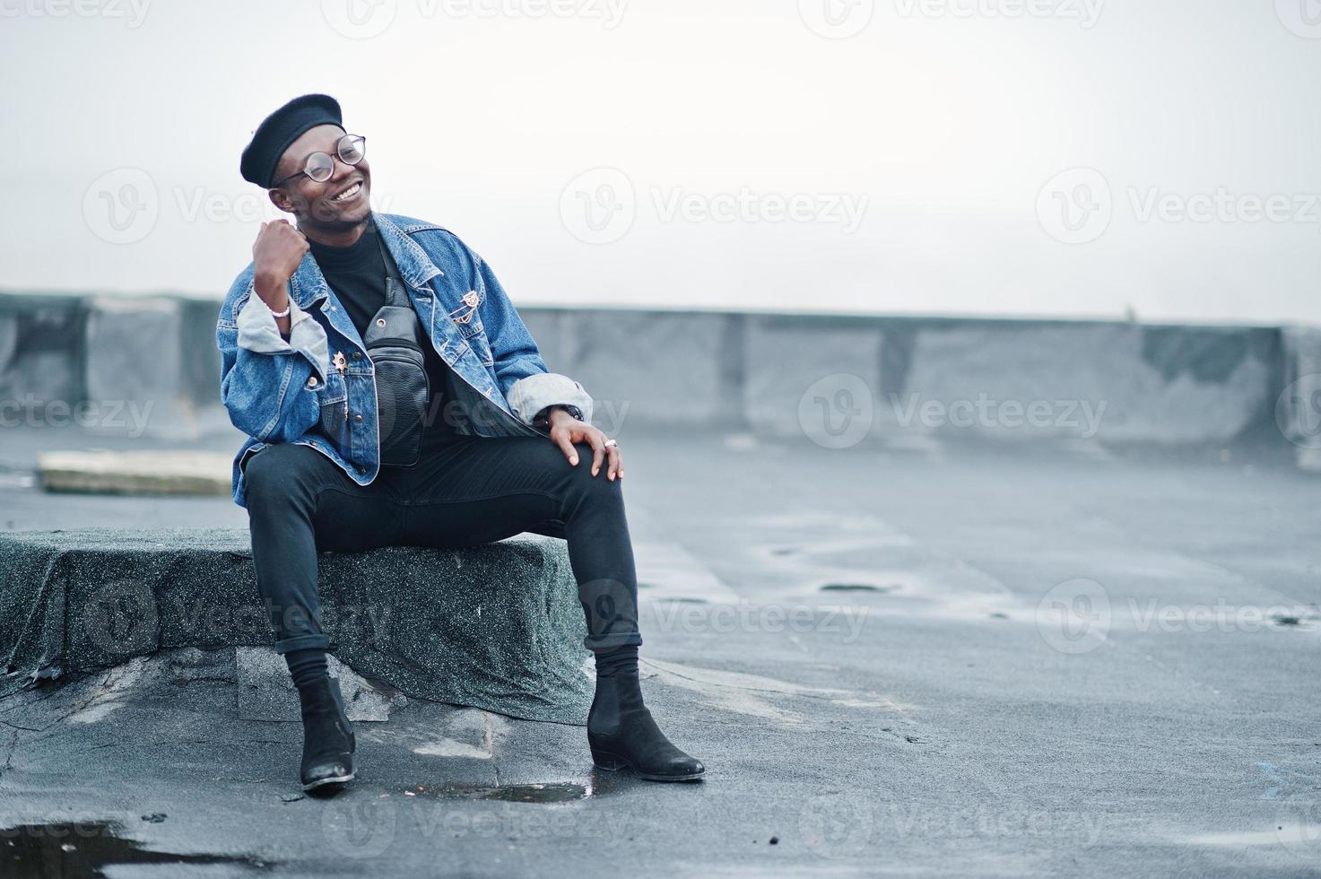 African american man in jeans jacket, beret and eyeglasses posed on abandoned roof. photo