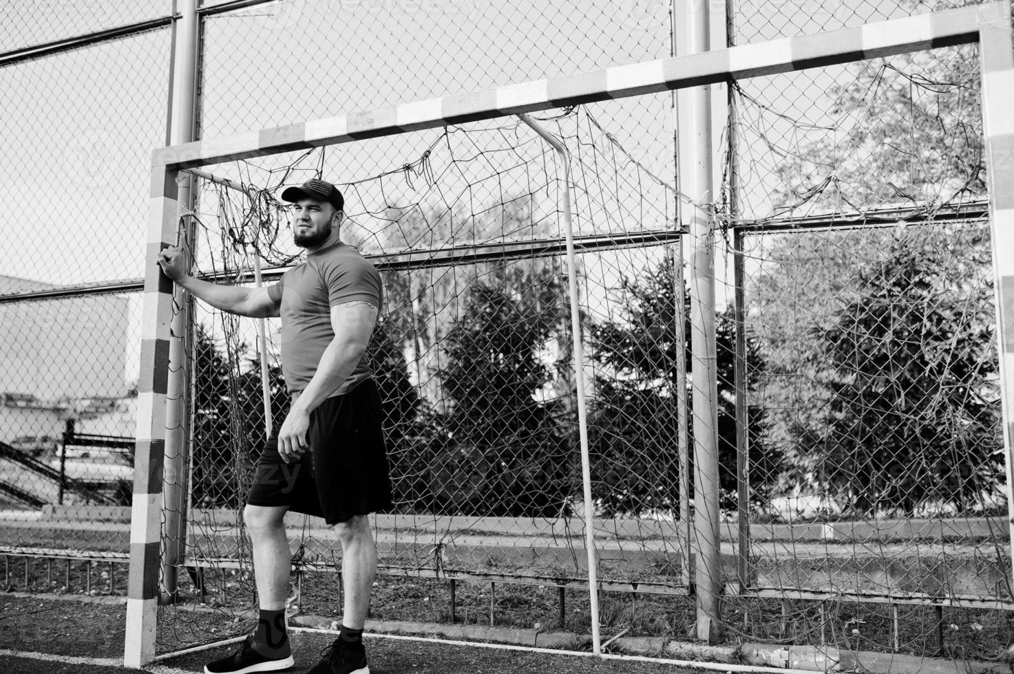 Young brutal bearded muscular man wear on red shirt, shorts and cap at stadium. photo