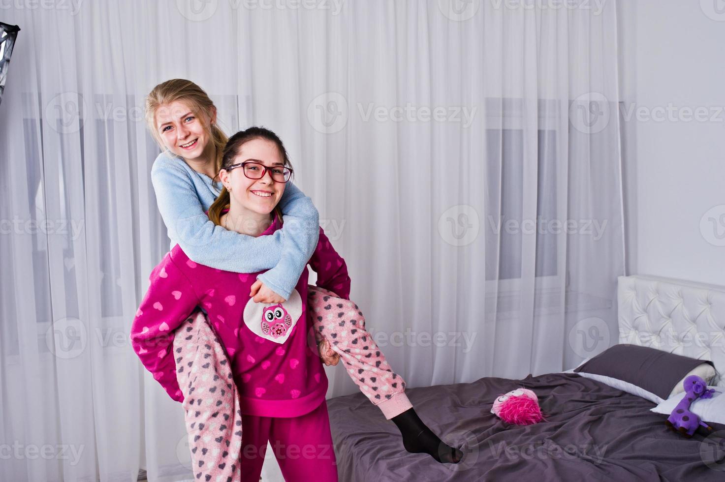 Two friends girls in pajamas having fun on bed at room. photo