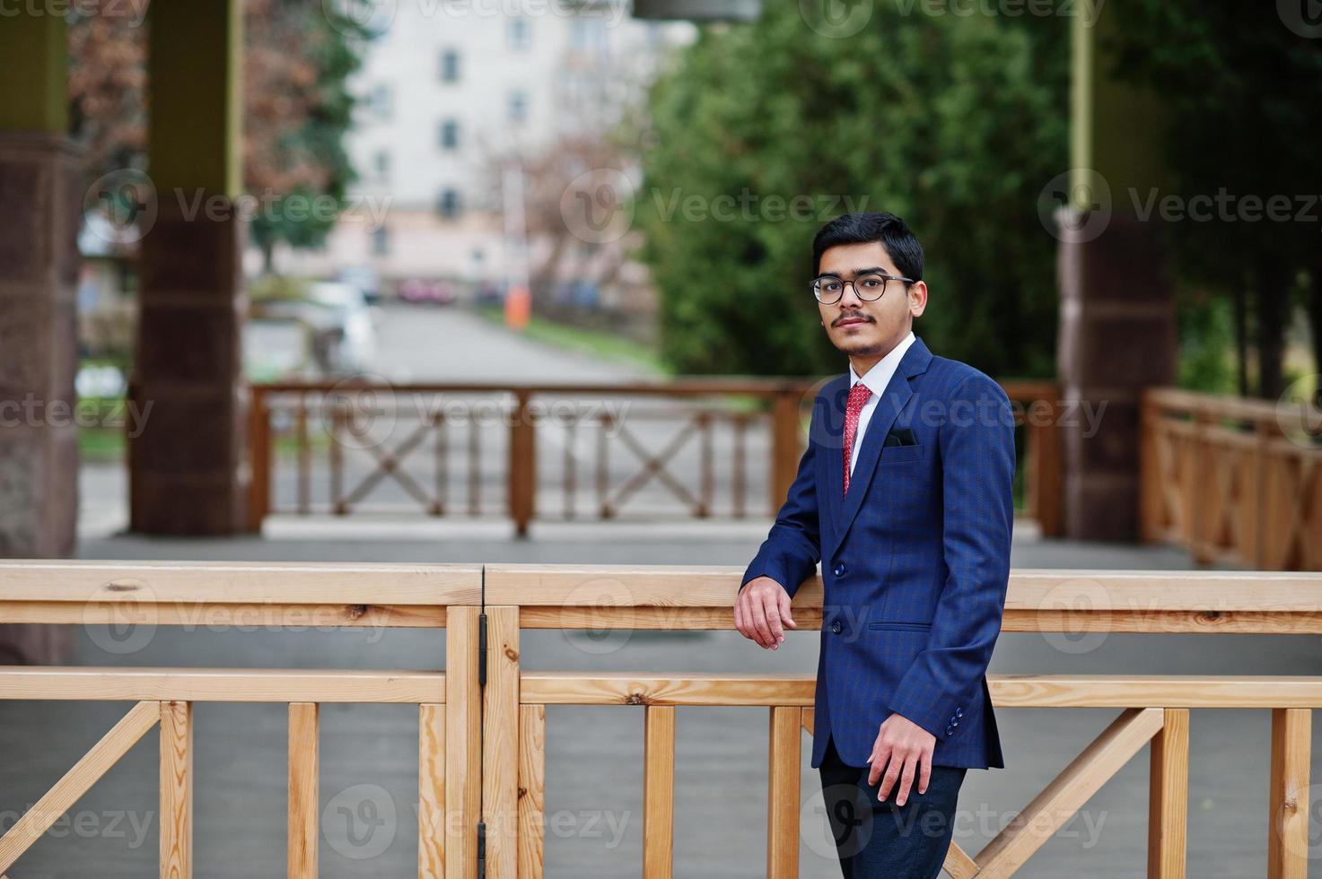 Indian young man at glasses, wear on suit with red tie posed outdoor. photo