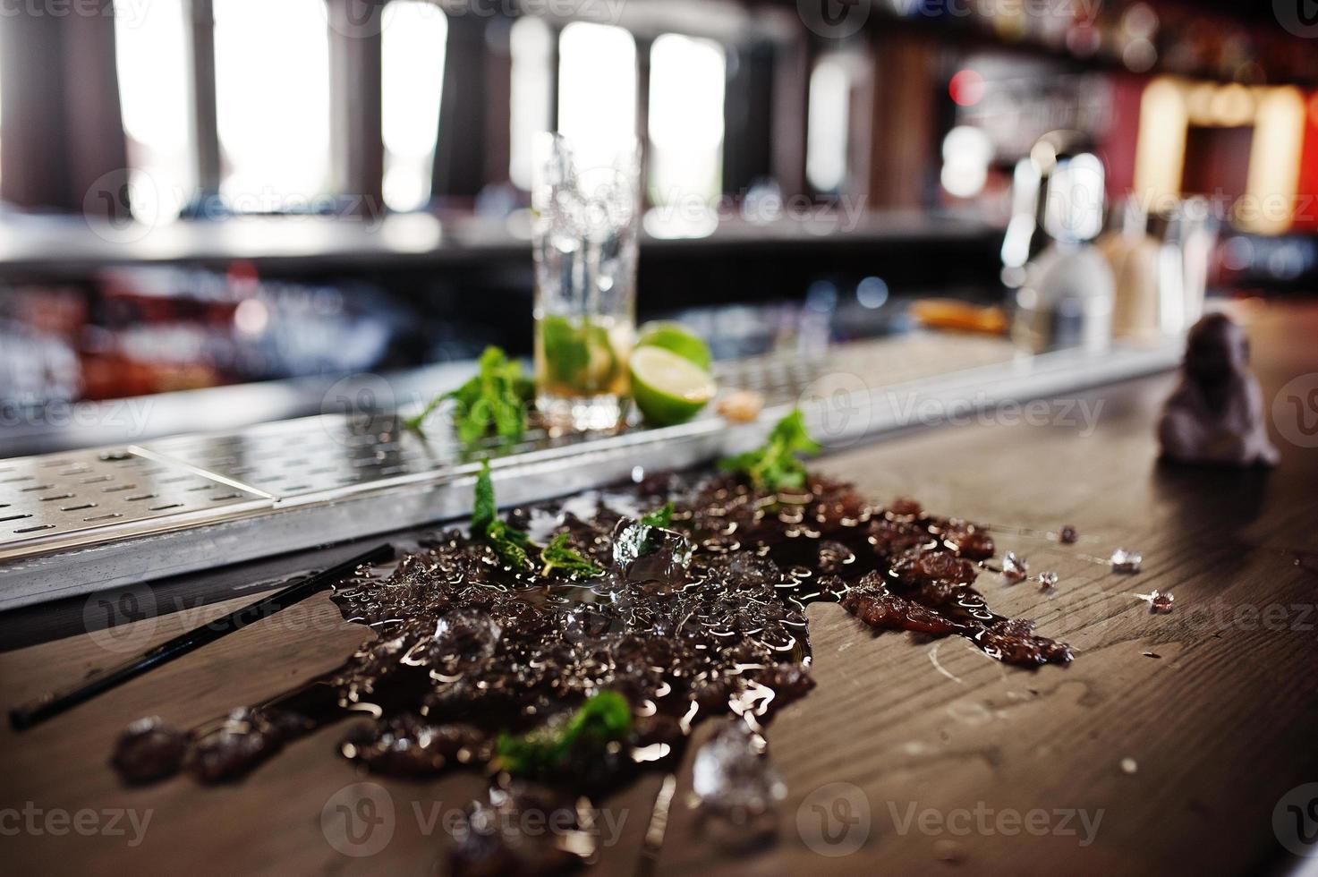 Alcoholic spilled coctail with mint and ice at bar table. photo
