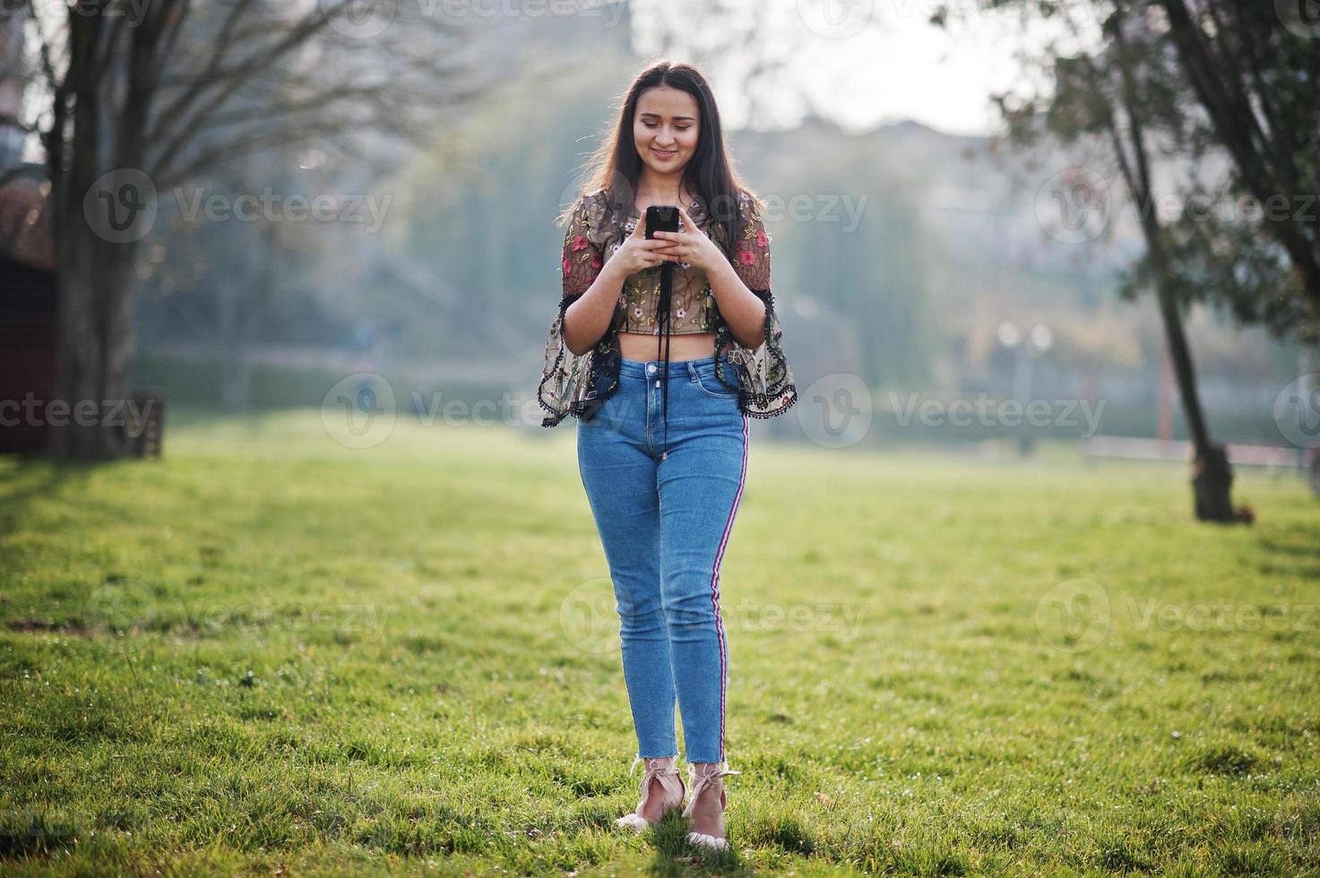 Pretty latino model girl from Ecuador wear on jeans posed at street with mobile phone. photo