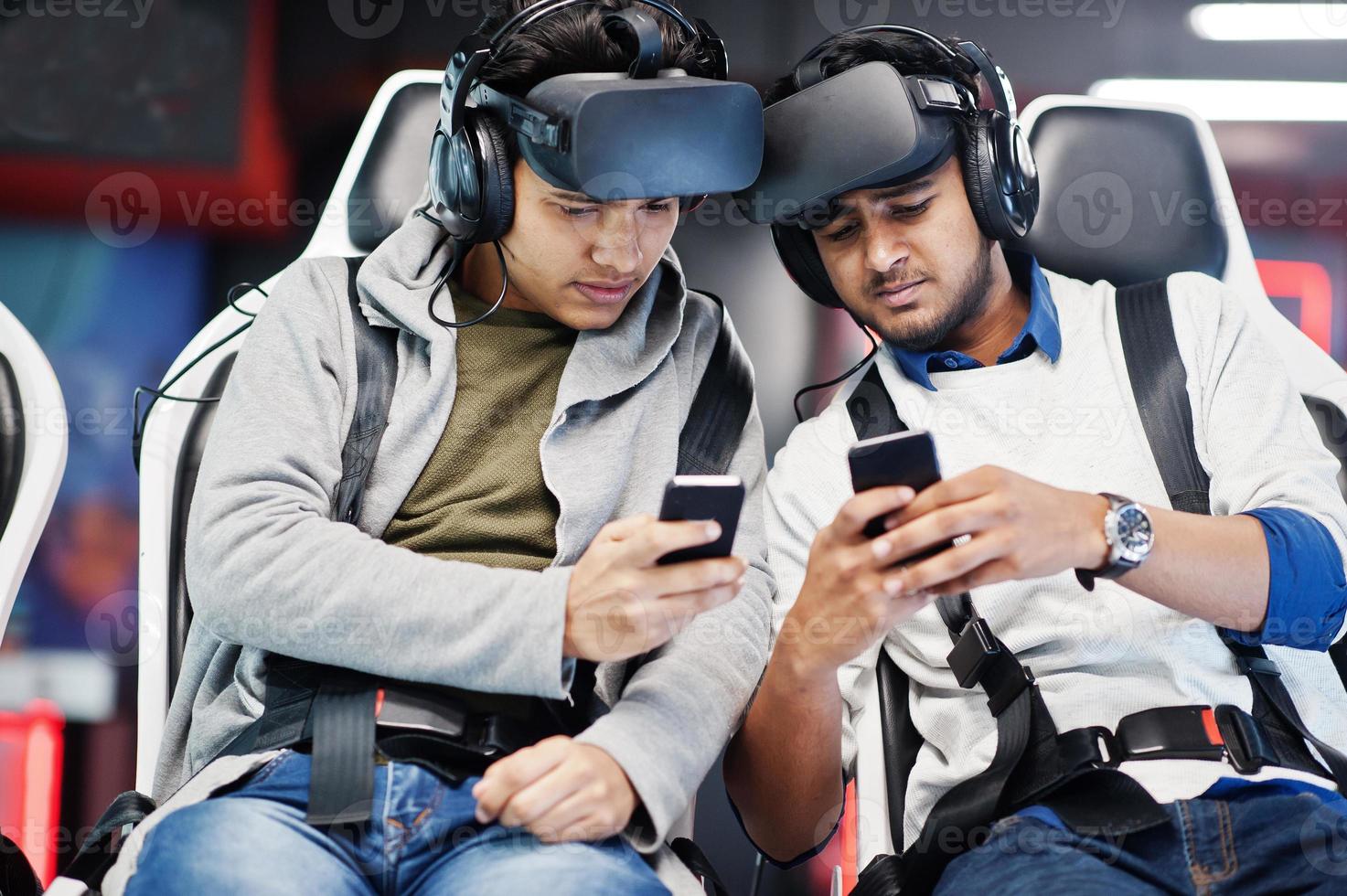 Two young indian people having fun with a new technology of a vr headset at virtual reality simulator with mobile phone at hands. photo