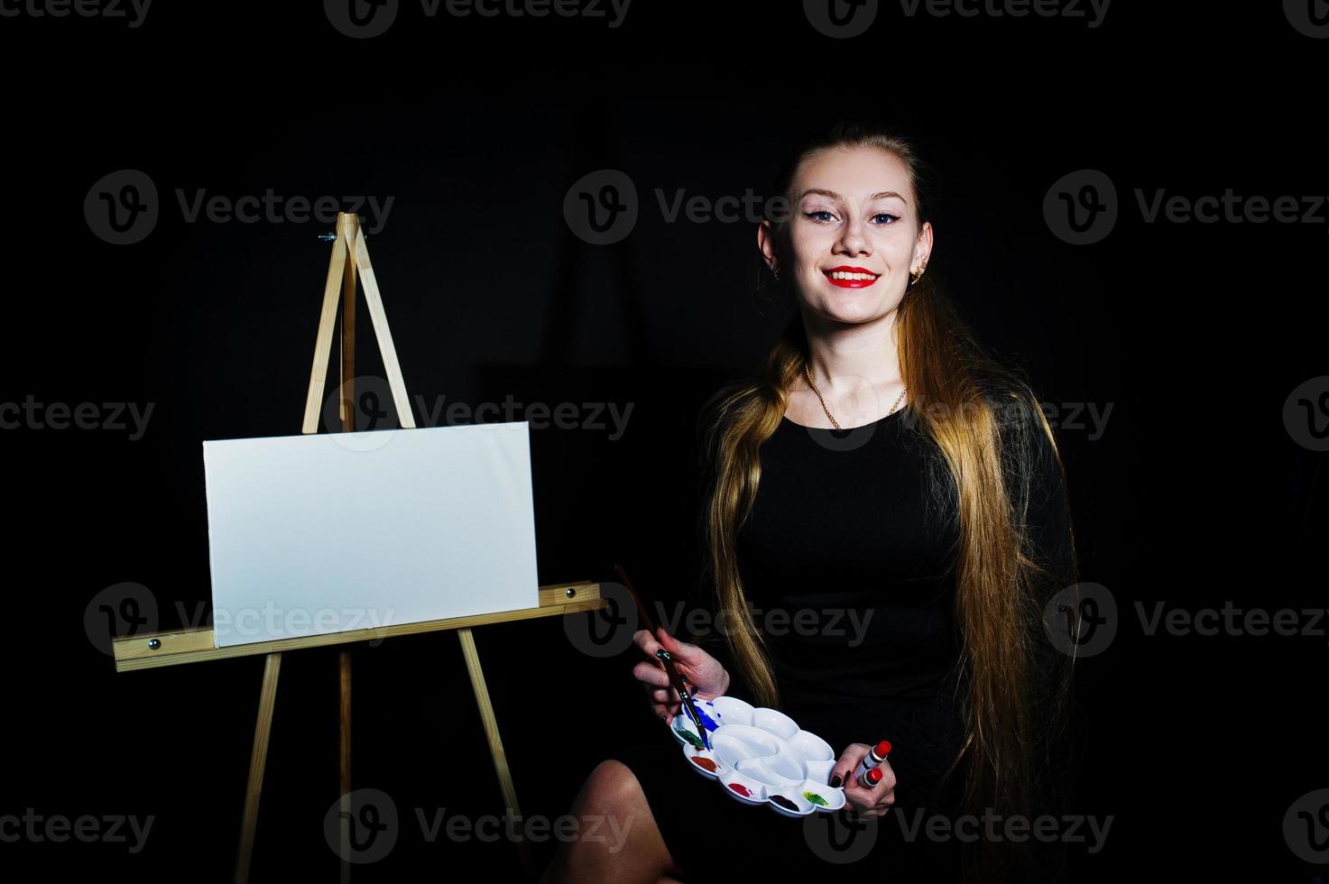 Beautiful woman artist painter with brushes and oil canvas posing in studio isolated on black. photo