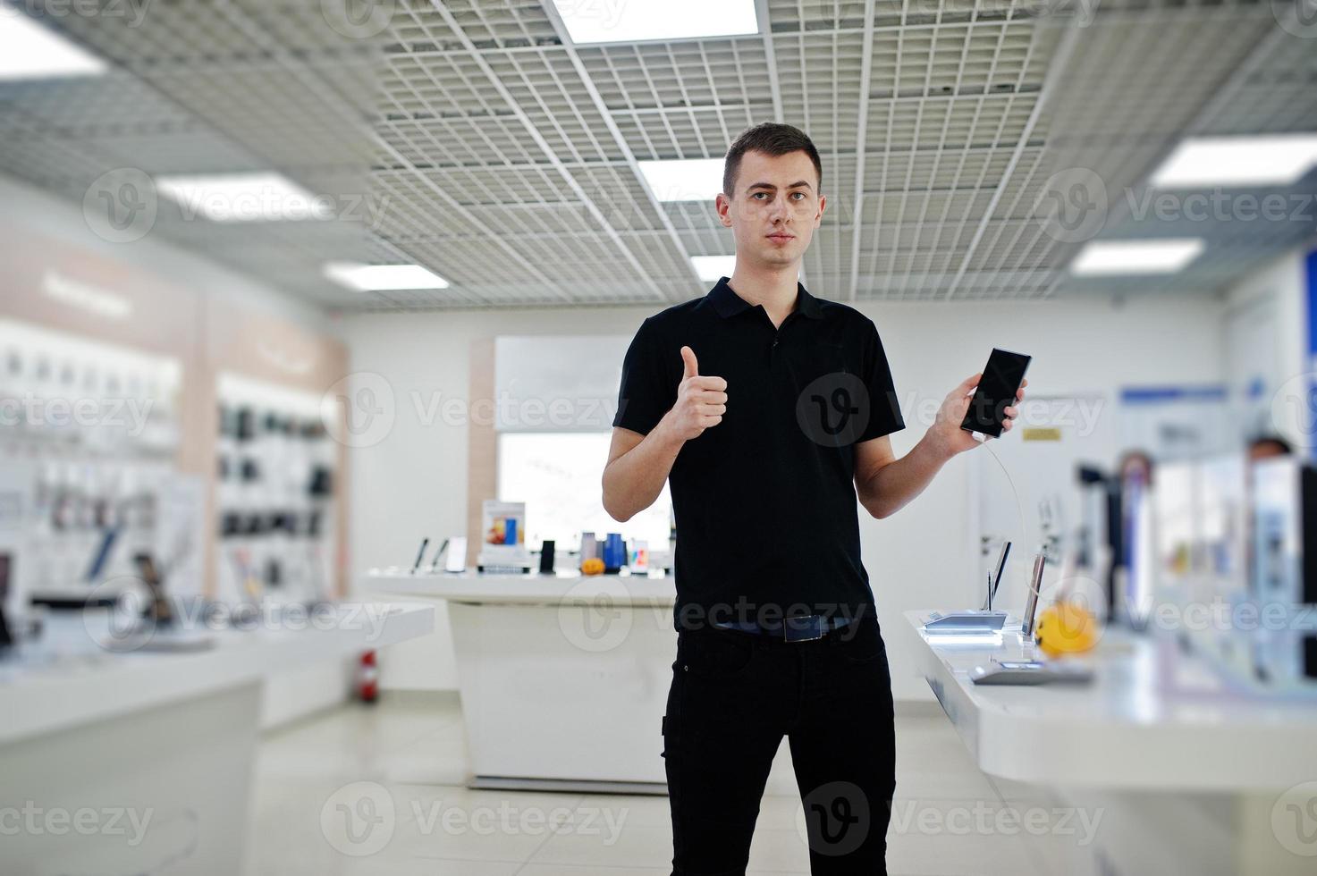 vendedor hombre consultor profesional de telefonía móvil en tienda de tecnología o tienda sostenga un nuevo teléfono inteligente a mano y muestre el pulgar hacia arriba. foto