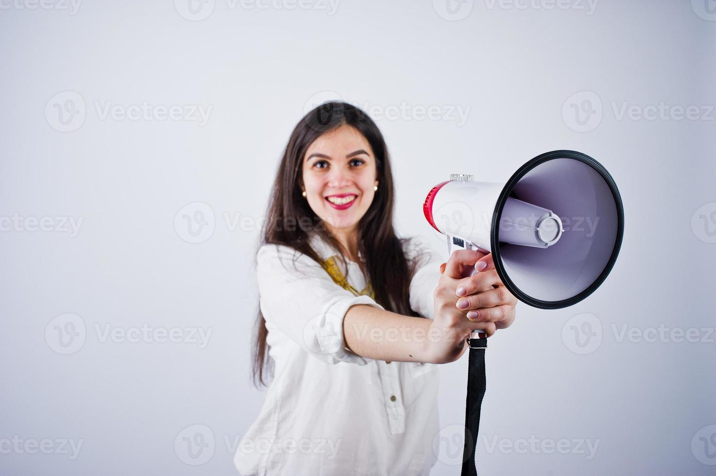 retrato de una mujer joven con pantalones azules y blusa blanca posando con megáfono en el estudio. foto