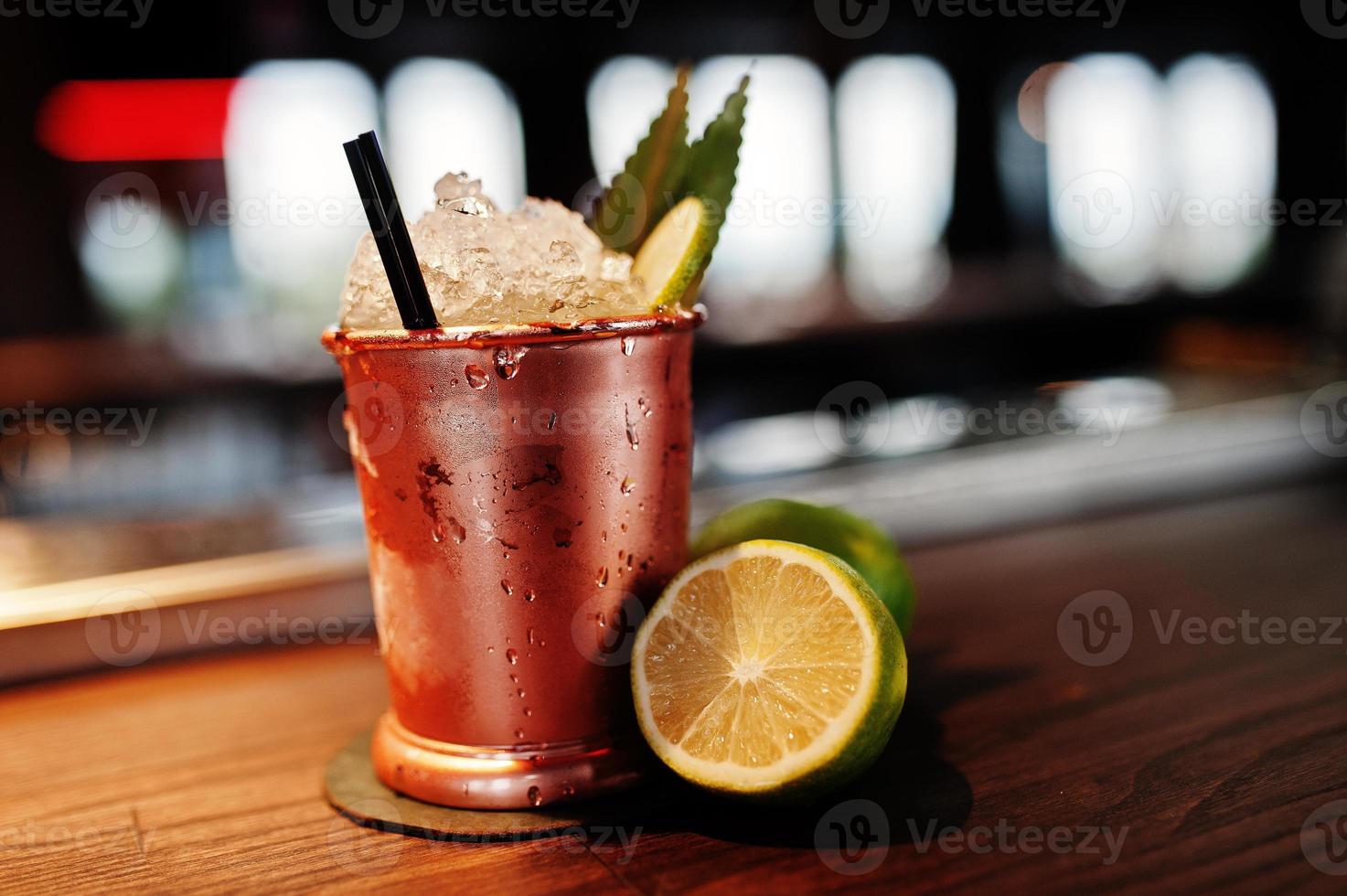 cóctel alcohólico con hielo y limón en lata de bronce en la mesa del bar. foto