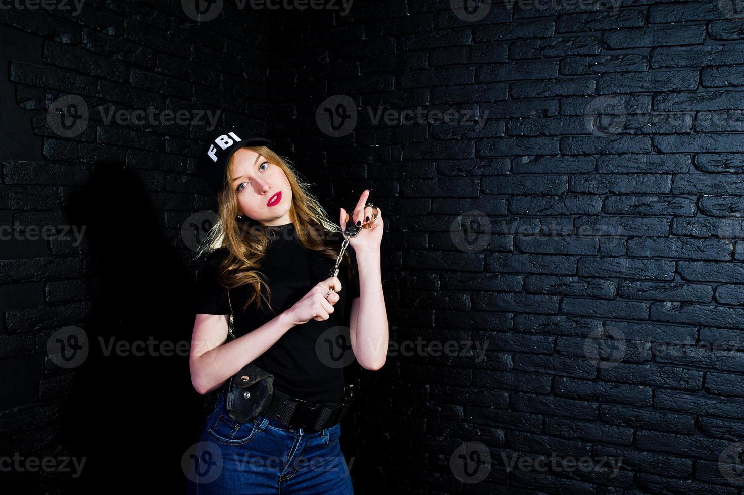 FBI female agent in cap and with gun at studio against dark brick wall. photo